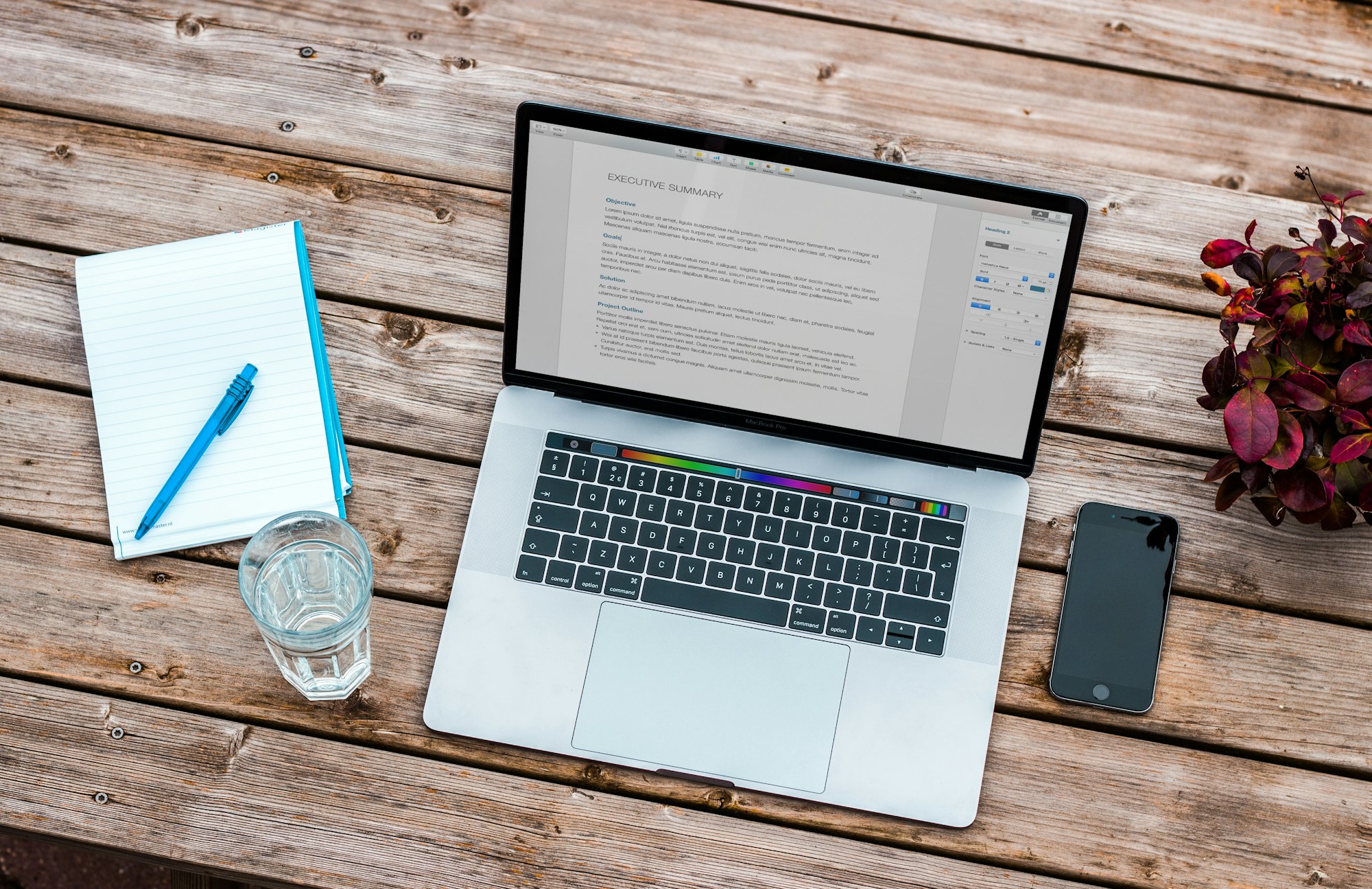 MacBook on a wooden desk with a notepad and an iPhone