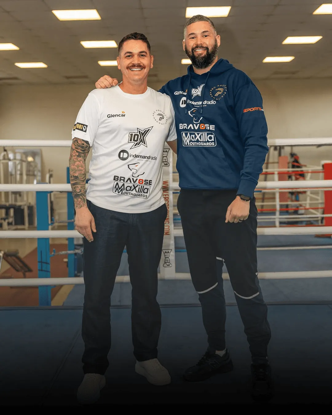 Two men in a boxing ring, one in a white shirt, one in a hoodie.