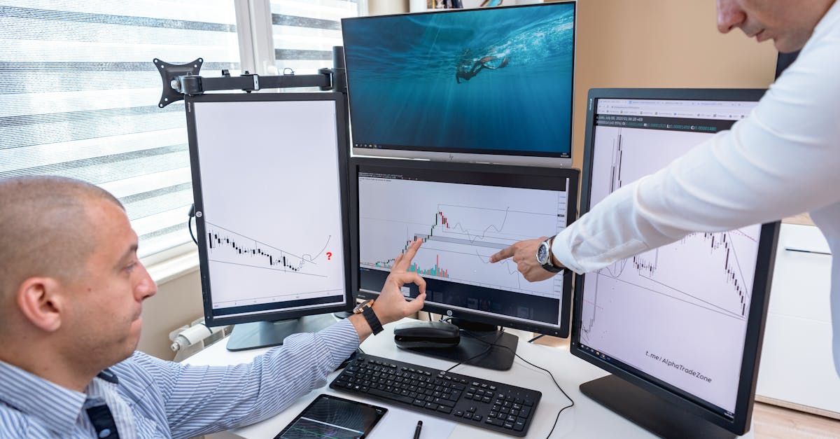 Two business professionals analyzing financial data on multiple computer screens in an office settin