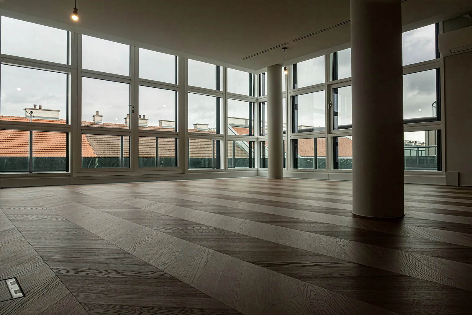 Großer, leerer Innenraum mit bodentiefen Fenstern und frisch verlegtem Parkettboden; moderne, helle Raumgestaltung