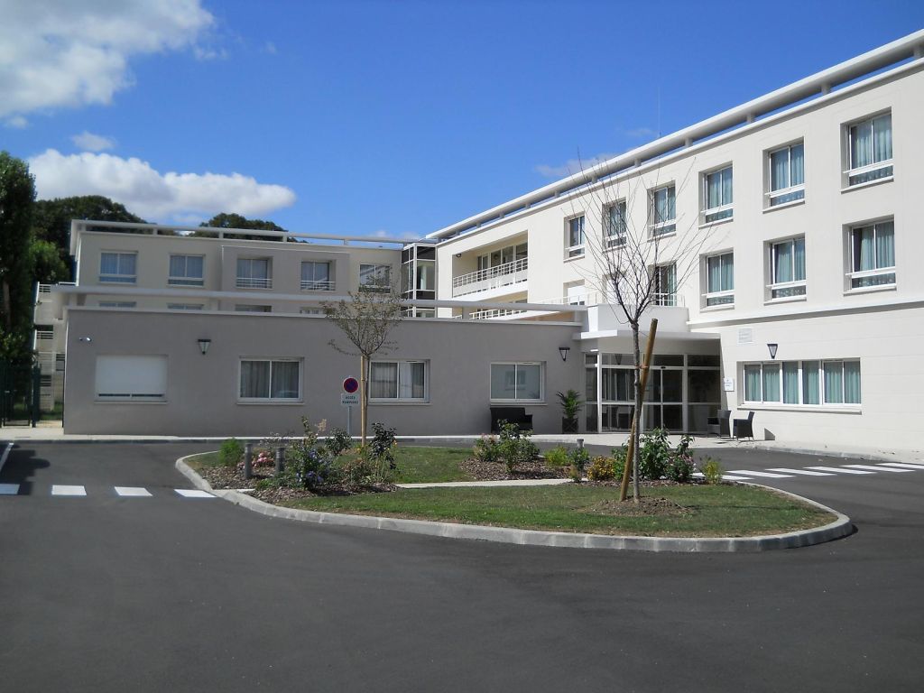 Modern white multi-story residential building exterior with clear blue sky, landscaped grounds, and paved driveway