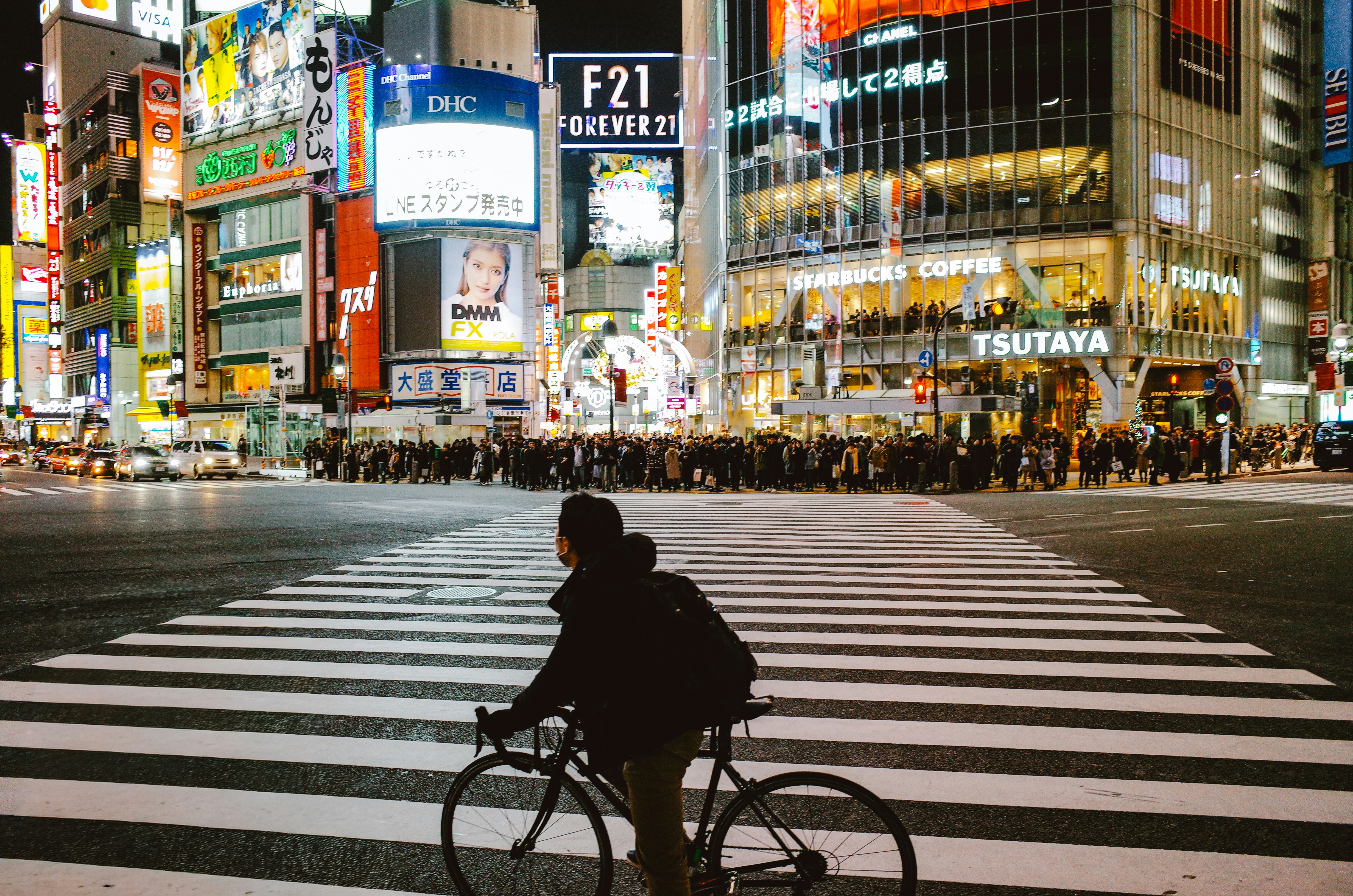 Man on bicycle crosses busy shibuya street at night
