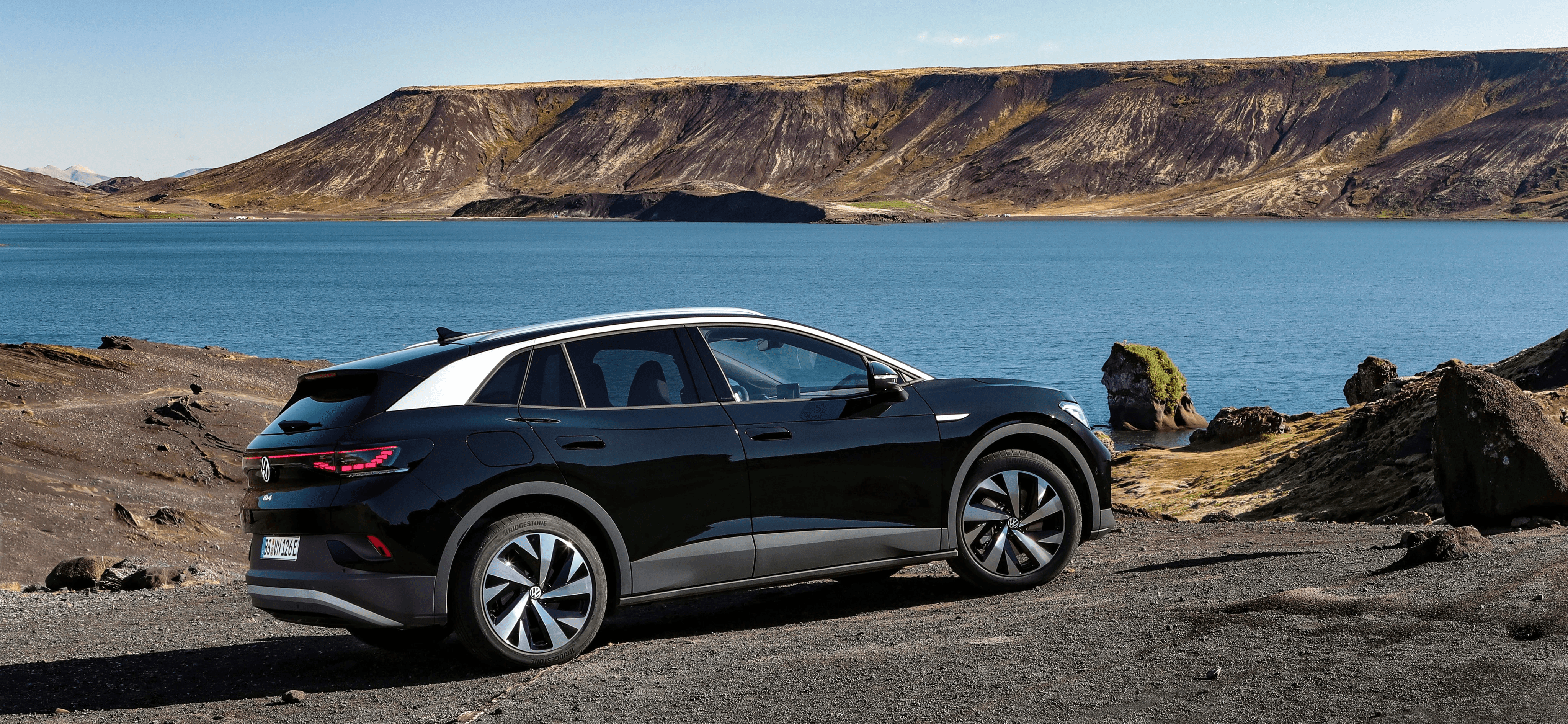 Volkswagen ID.5 noire face à un lac et des reliefs volcaniques, SUV coupé électrique dans un décor naturel