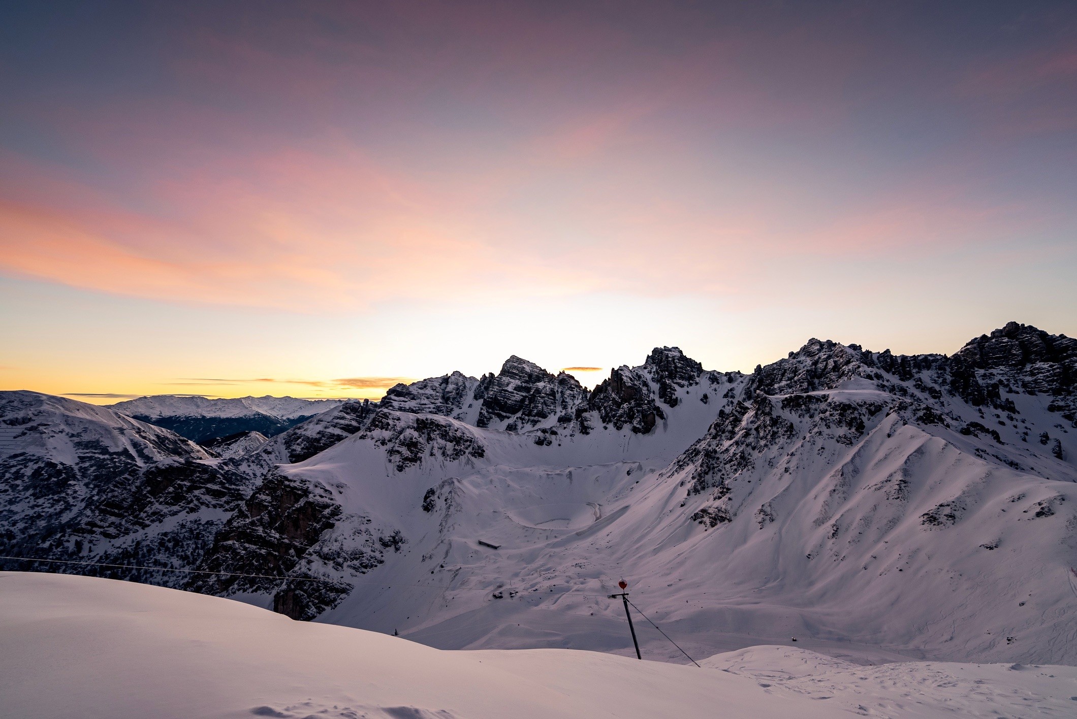 Snow-covered mountain peaks at sunrise with colorful sky.