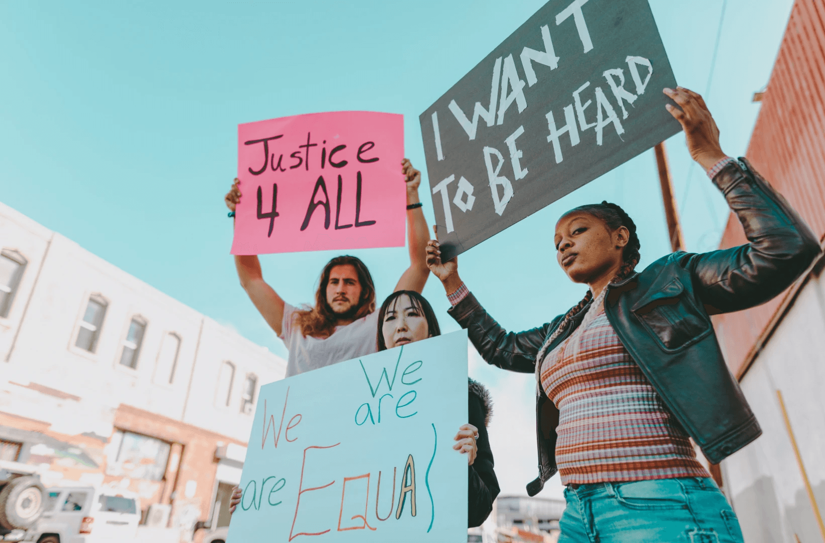 Two individuals hold signs while participating in a protest under a clear blue sky.