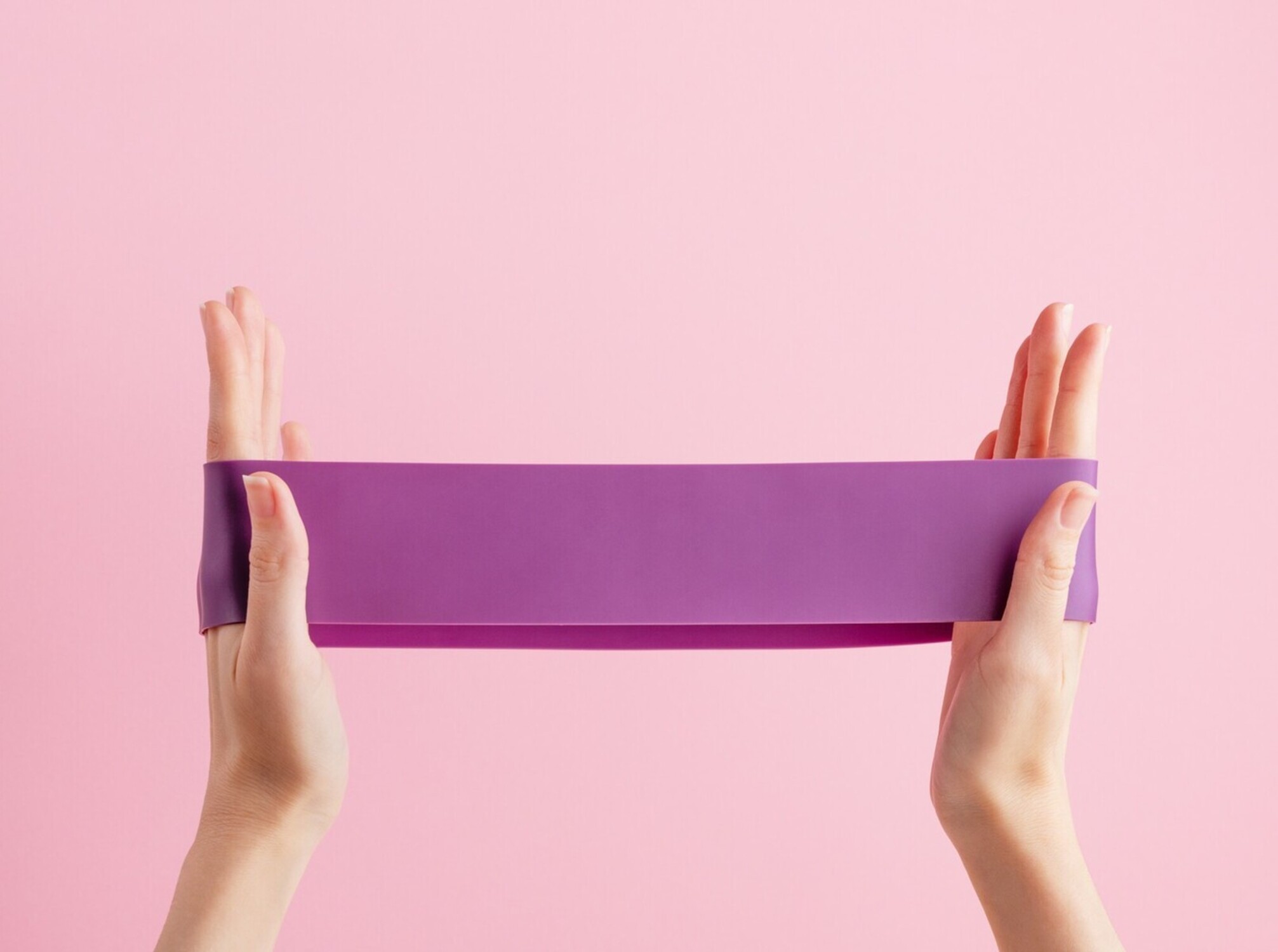 woman holding up a resistance band with her hands to show an example of the best home exercise equipment for weight loss