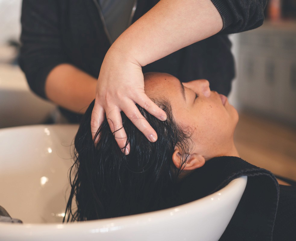 Client receiving a relaxing scalp massage, shampoo, and scalp treatment at the salon sink, highlighting the pampering and care-focused service experience.