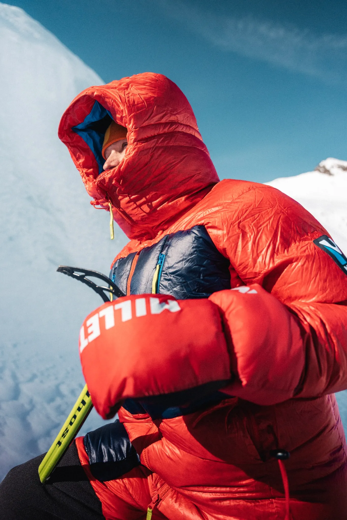 Portrait d’alpiniste en doudoune Millet rouge, équipé pour le froid extrême en haute montagne.