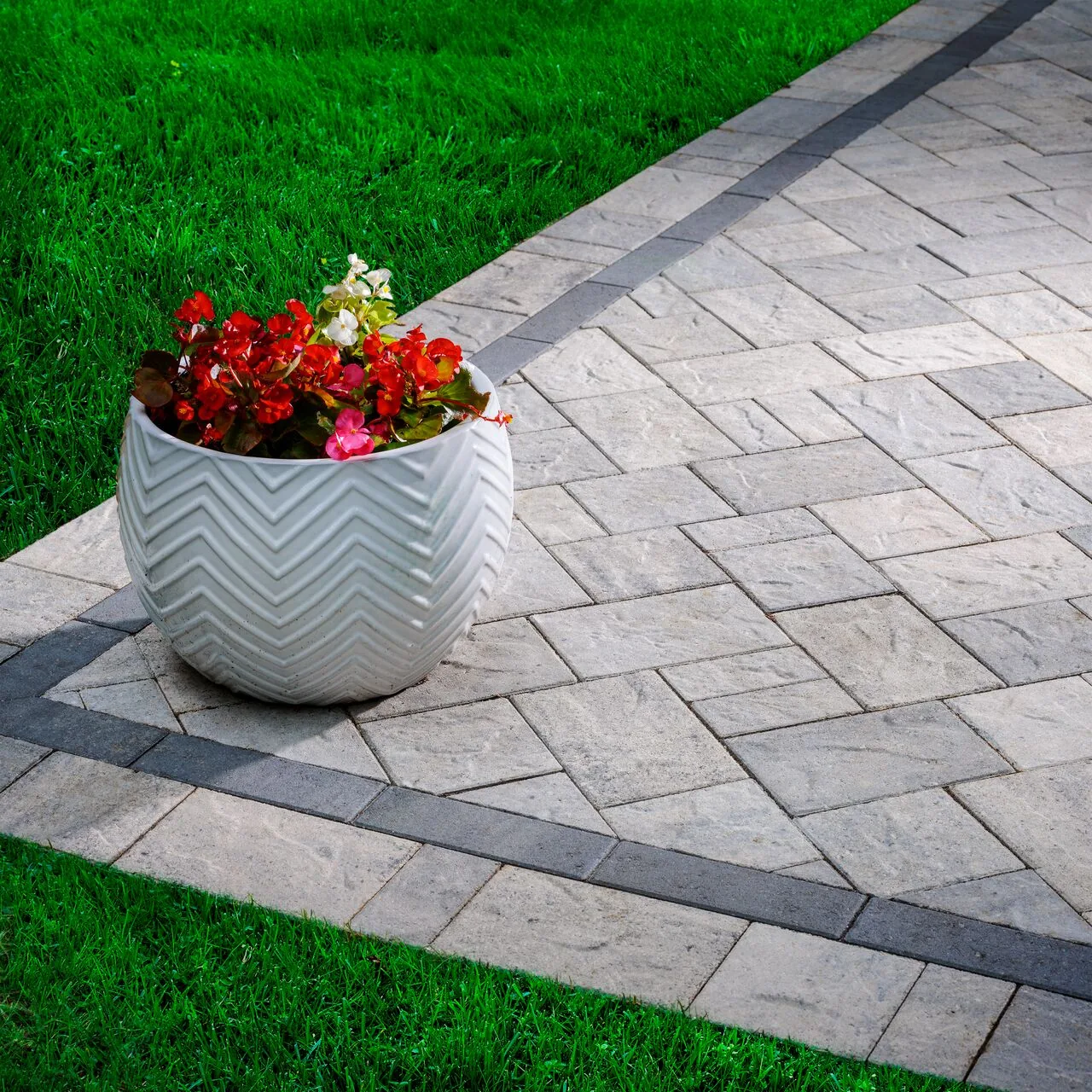 Small details, clear edges Light rectangular paving with dark border bands beside lawn and a flower planter.