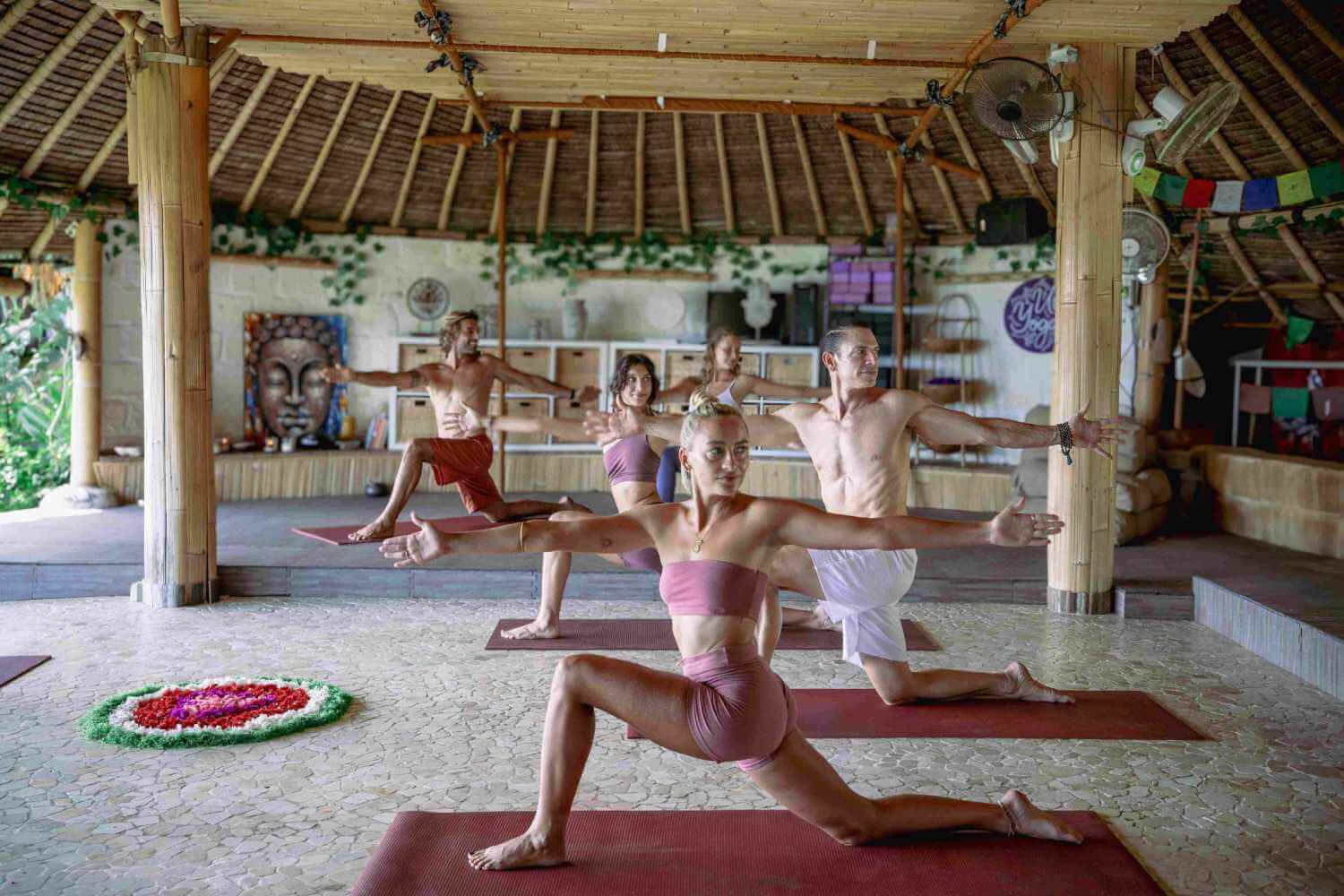 Students practicing Warrior II pose during a Hatha yoga class in the open-air bamboo shala.