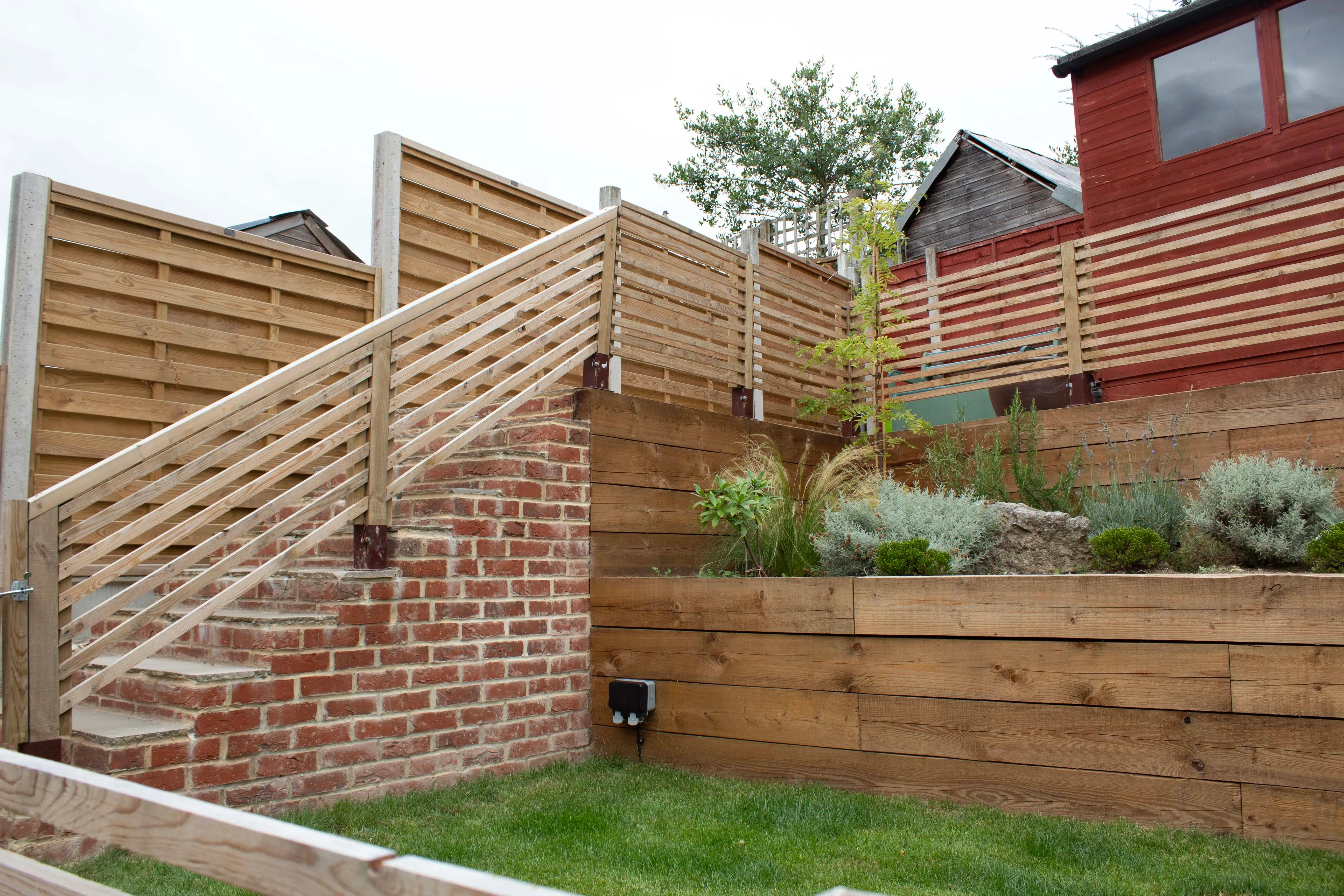 A modern outdoor staircase leads up to a raised garden, surrounded by wooden fencing and greenery.