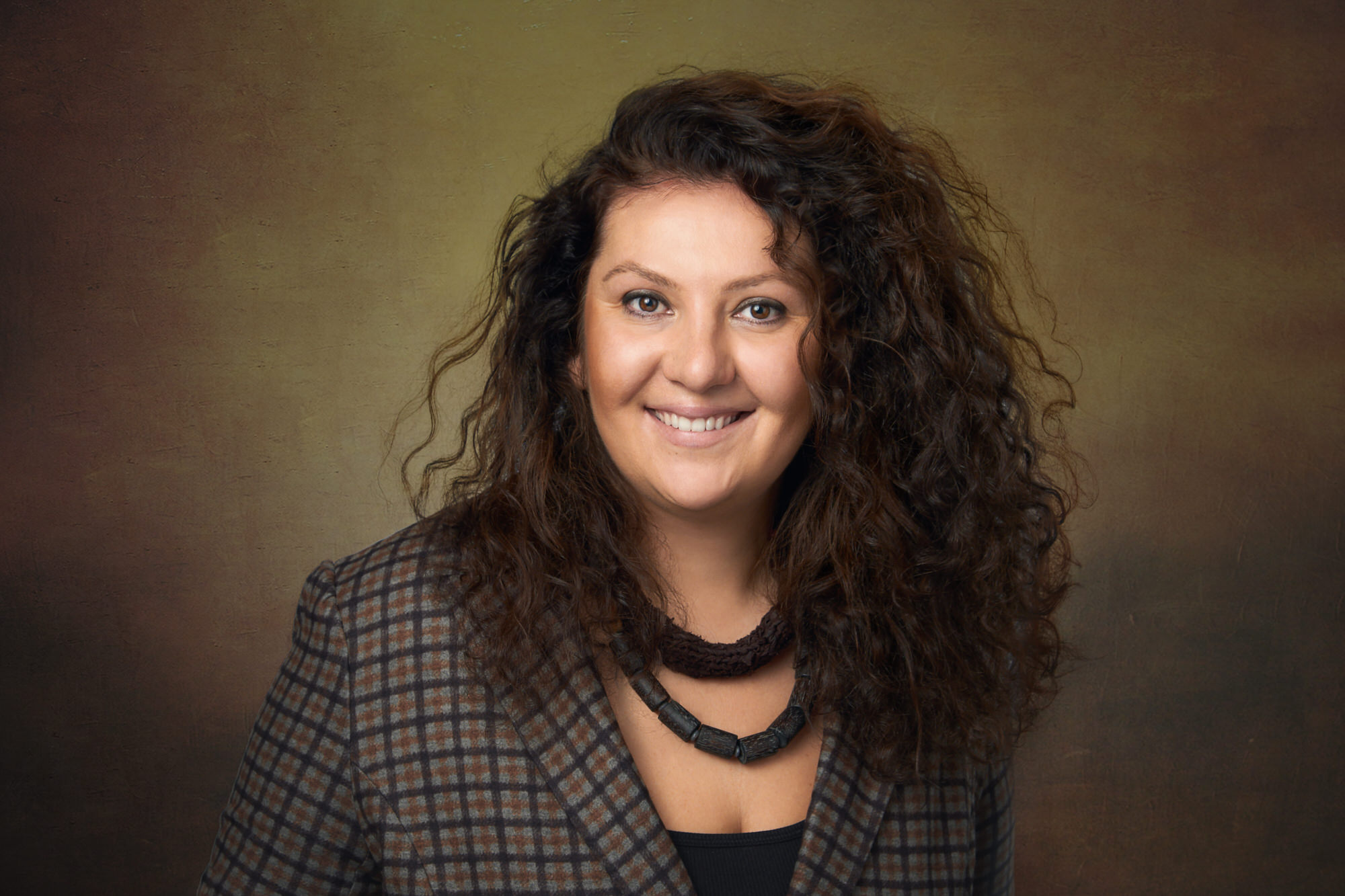 Professional photo of white woman with long curly hair in plaid blazer and chunky necklace