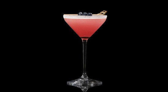 A closeup of a Blueberry Lemon Drop drink against a dark background.
