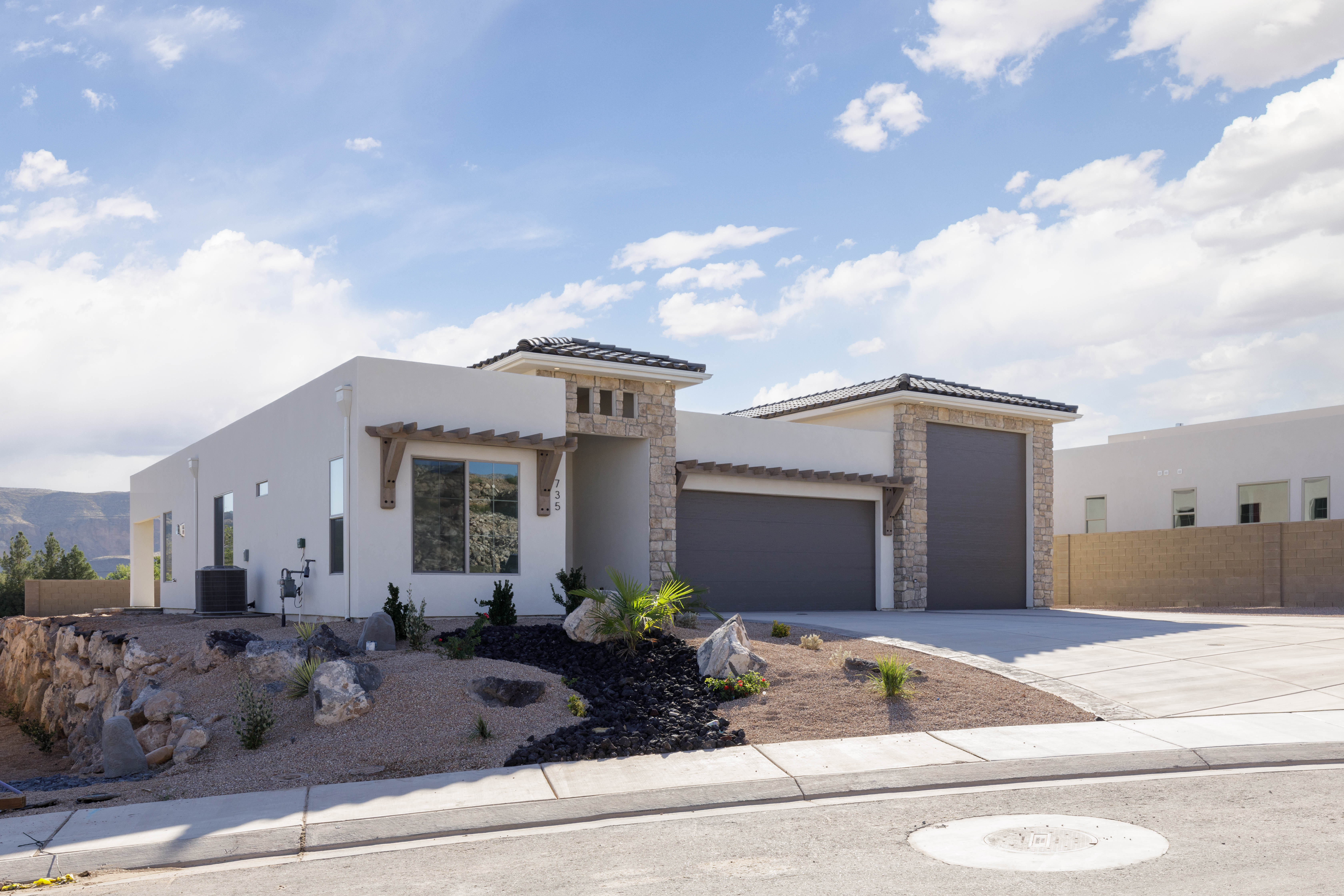 Custom home exterior with stucco, stone, wood accents, and an RV door with full landscaping in Hurricane, Utah.
