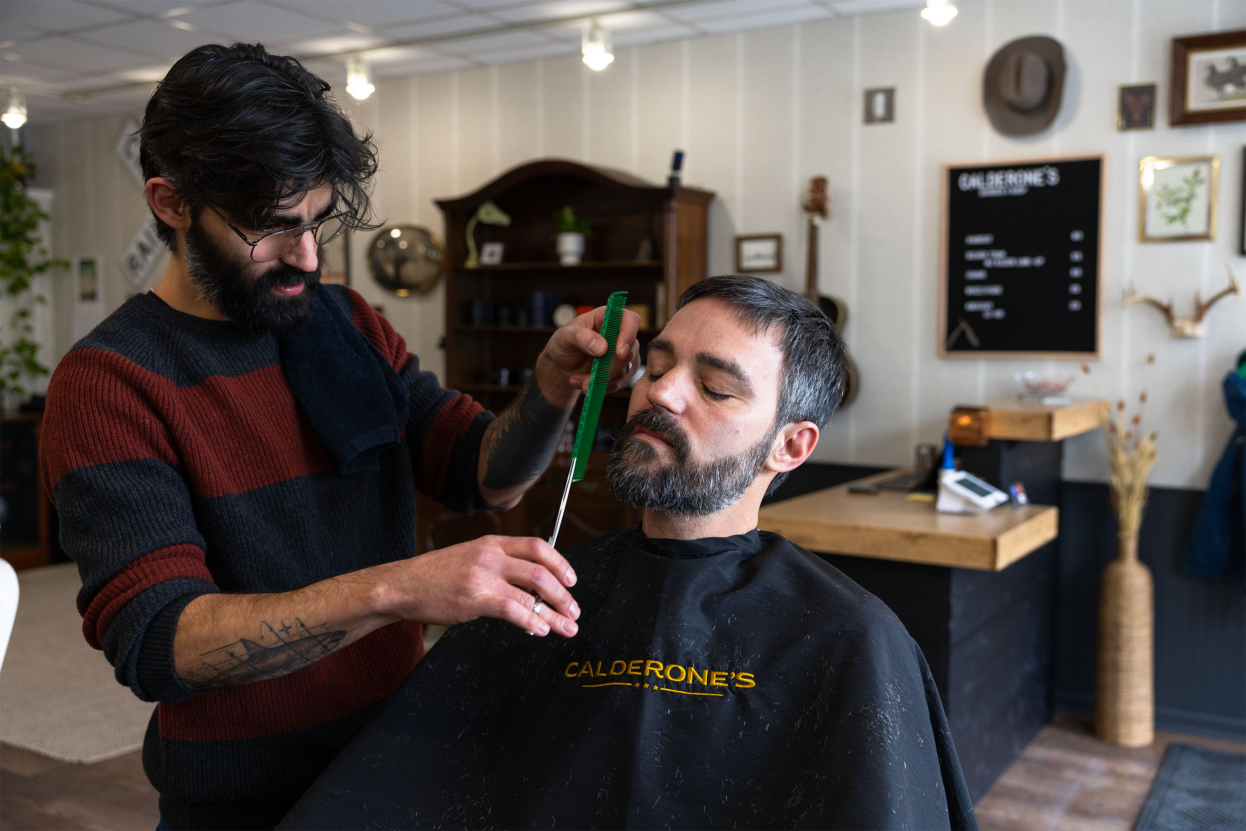 Barber trimming a client’s beard during a haircut appointment at Calderone’s Barbershop