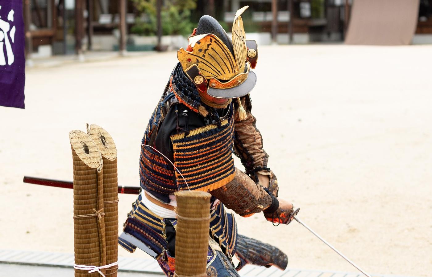 Japanese man wearing traditional samurai armor and demonstrating the use of a katana