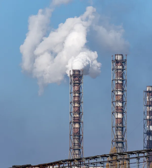 Smoke rising from tall industrial chimneys against a clear blue sky