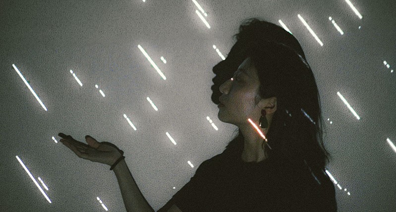 A photo of two girls seen from a side and holding a palm while some illuminated white lines fall like rain.