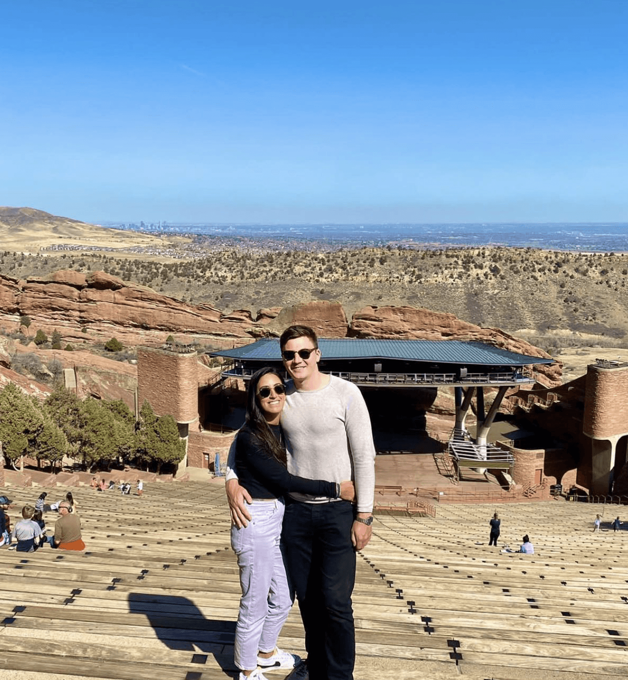 A close-up of two people holding hands, one wearing a denim jacket. The background is softly blurred, suggesting a tender, intimate moment in warm light.
