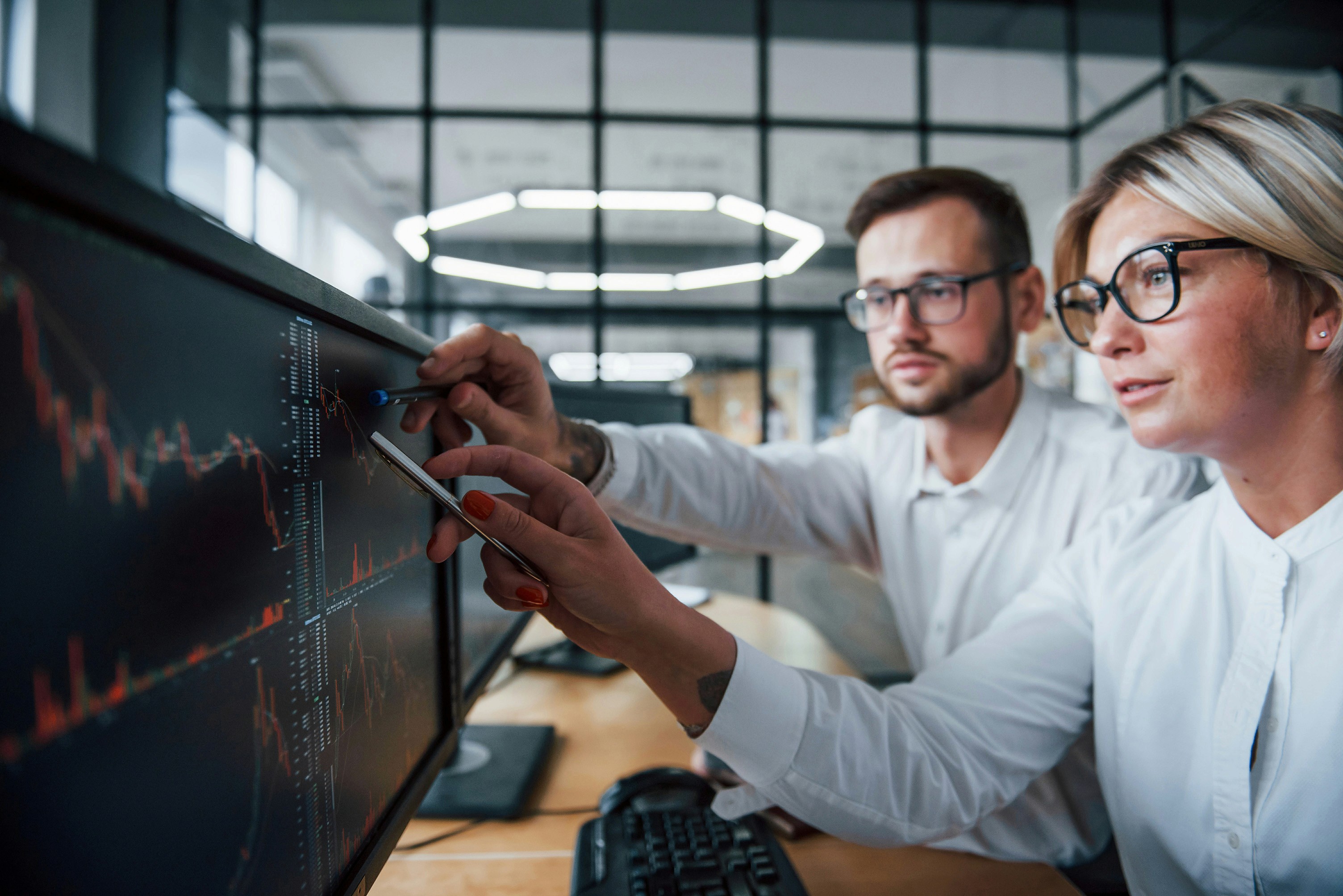 A male and female financial analyst viewing financial graphs on a monitor in a modern office