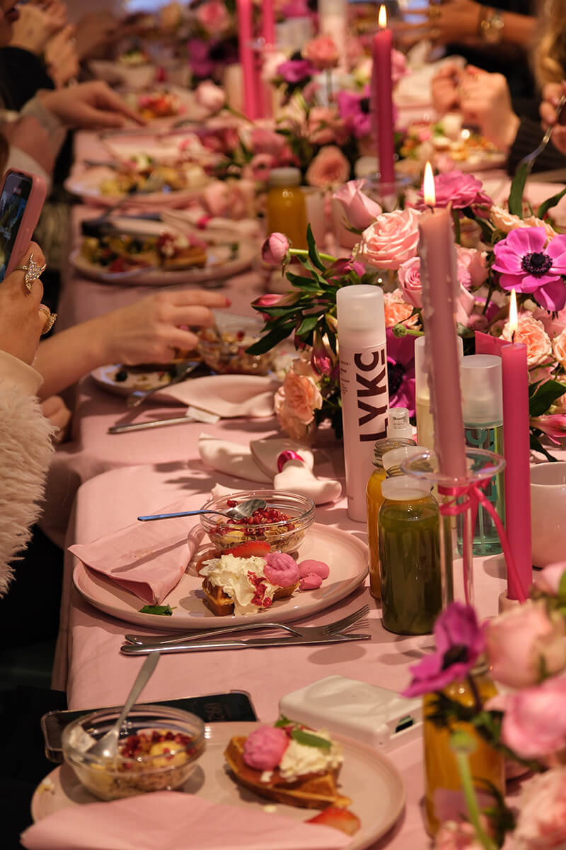 People eating food at a long table with candles and flowers placed on the table