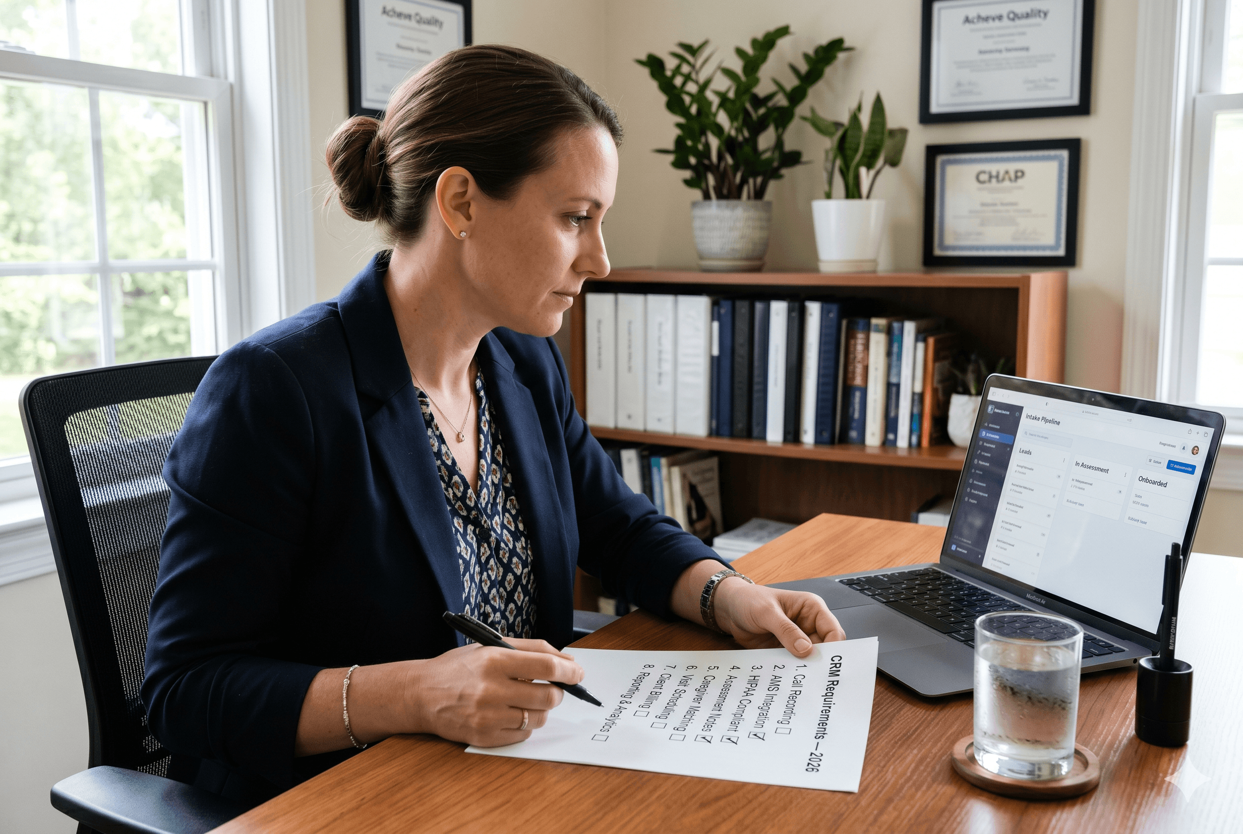 A home care agency owner in her early 40s sits at a clean desk, reviewing a printed "CRM Requirements — 2026" checklist beside an open laptop displaying an "Intake Pipeline" dashboard.