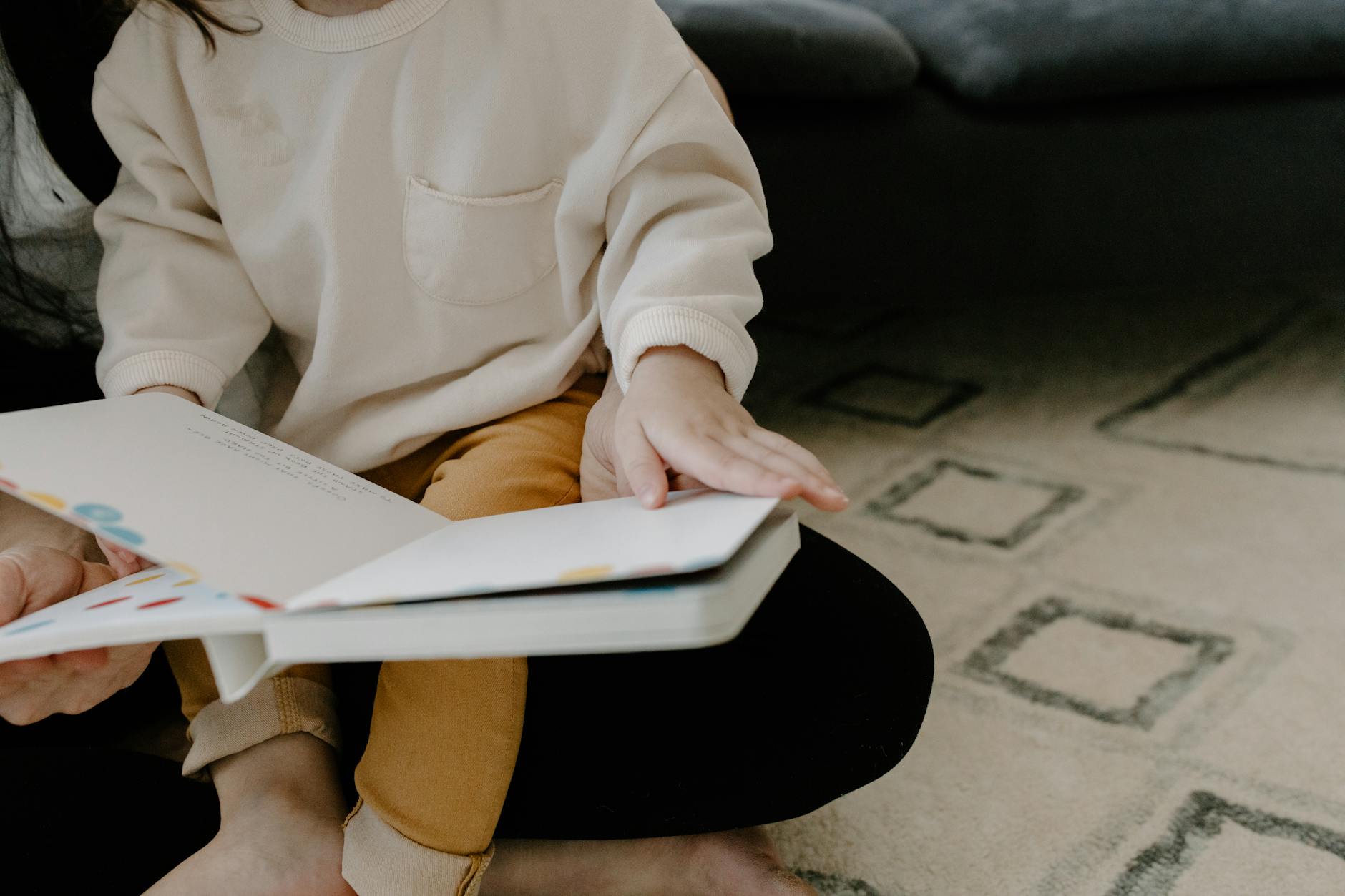 A toddler's small hands touching a fuzzy textured patch inside a bright board book with sensory elements.