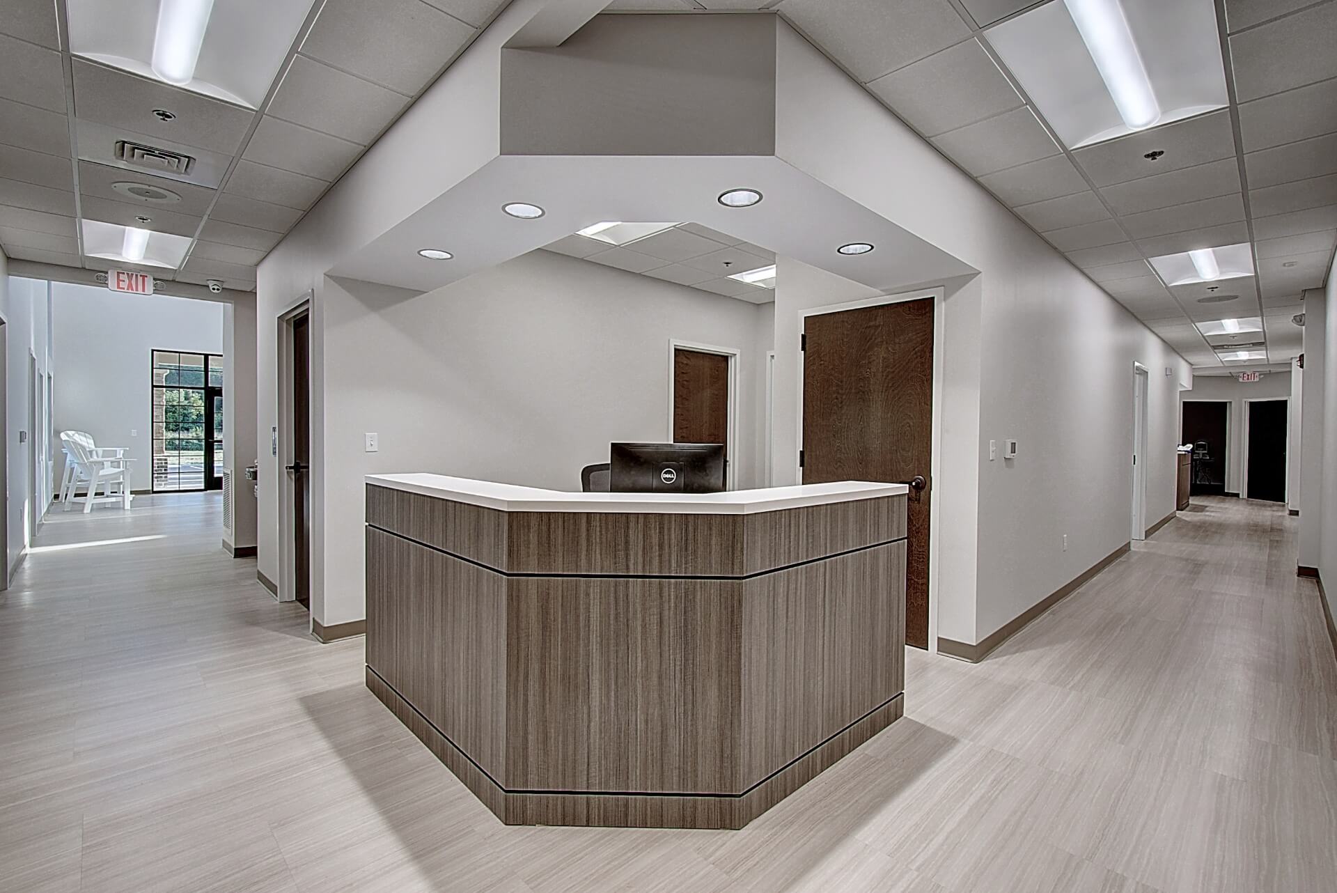 Modern reception area with a wooden front desk and sleek white walls, featuring bright overhead lighting.