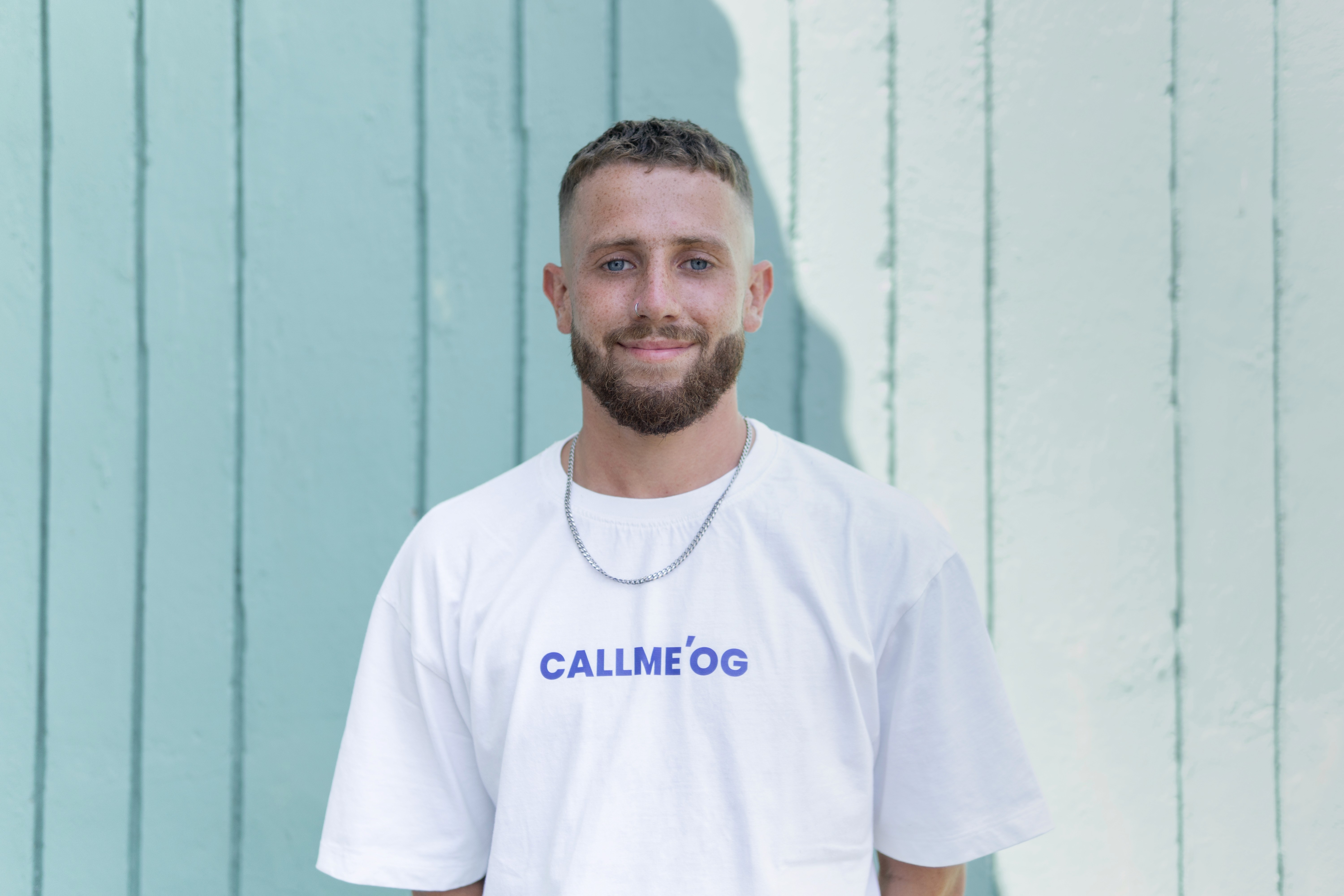 Person wearing a blue puffer jacket and red backpack standing in front of a light blue building on a city street.