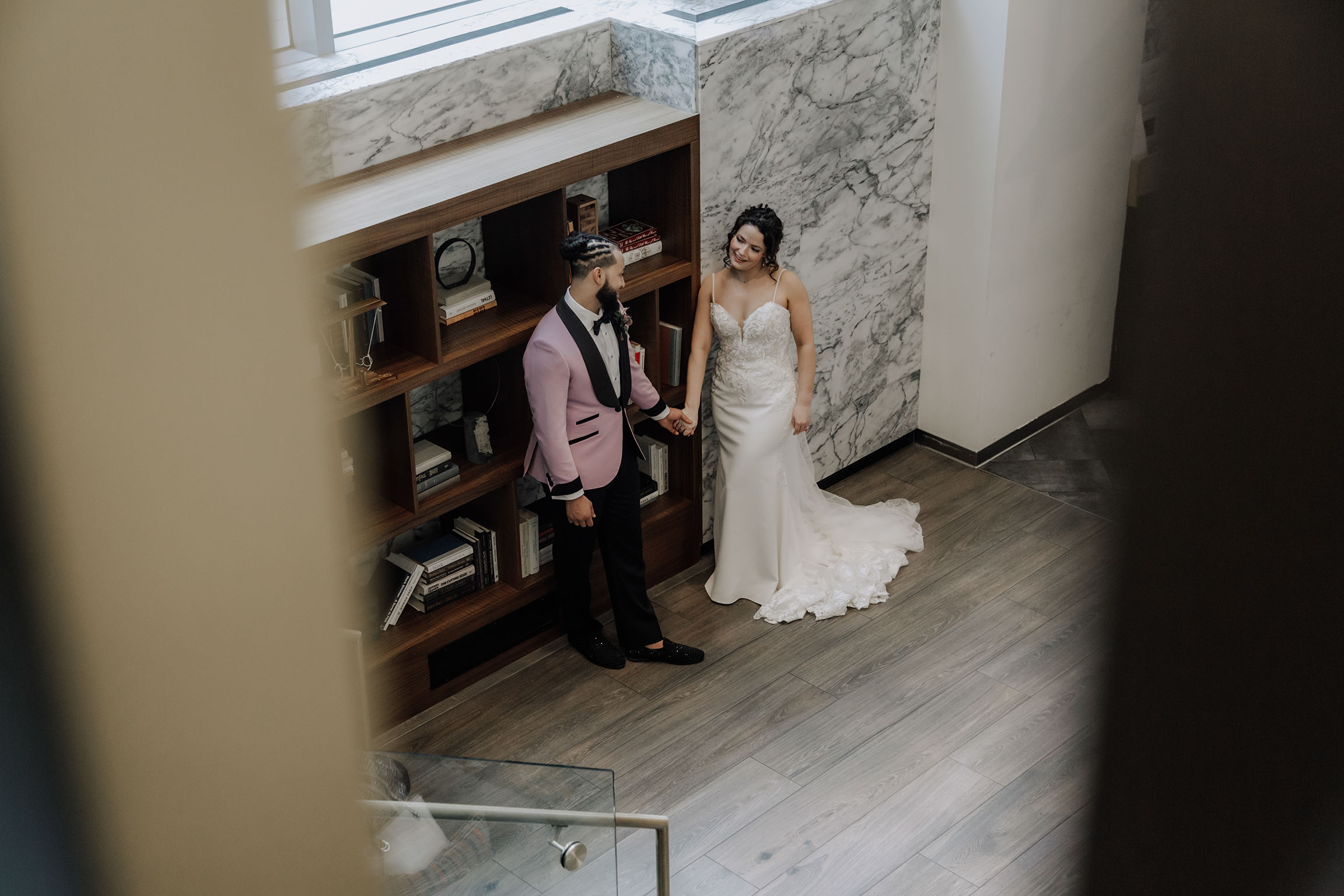 Newlyweds embracing in a quiet hallway framed by marble and wood.