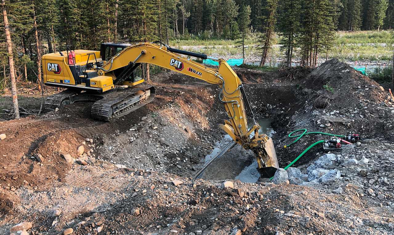 Wilco excavator conducting dewatering operations with pump system for flow gauge station construction on Elbow River