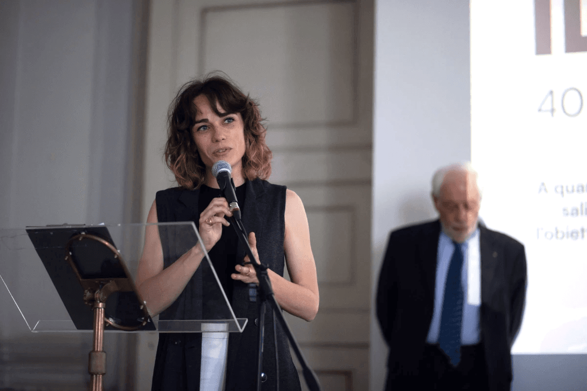 Giulia Caffaro su un podio mentre un uomo le sta dietro, in un contesto formale con uno sfondo chiaro.