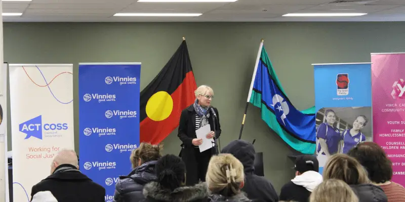 A speaker delivering a speach in front of the Aboriginal and Torres Strait Islander Flags. 