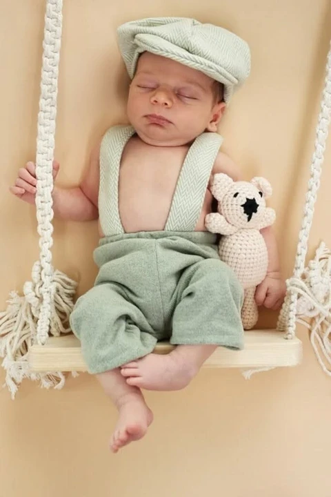 Newborn in a mint outfit and cap on a rope swing
