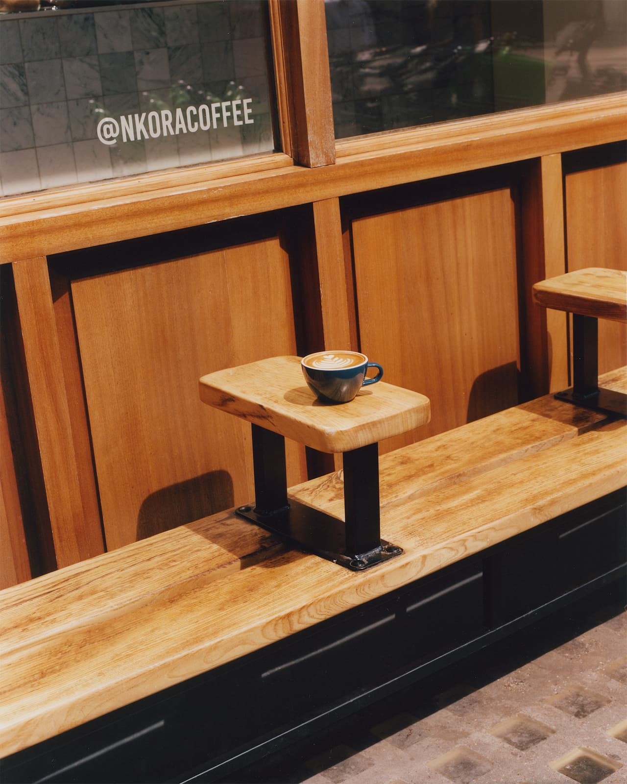Coffee Cup and Outdor Seating Bench in front of NKORA Mayfair Coffee Shop