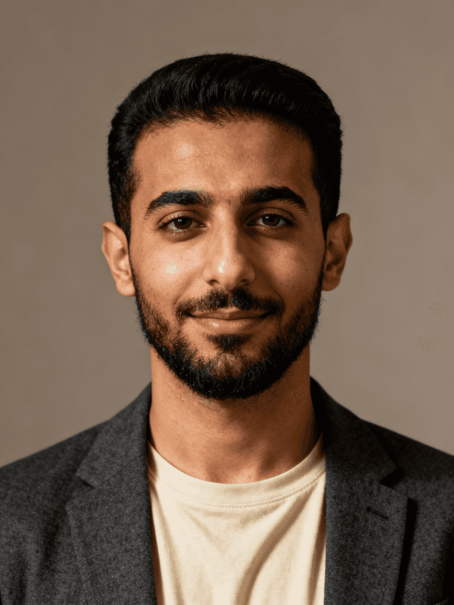 A smiling man with a beard and dark hair wears a gray blazer over a light shirt.