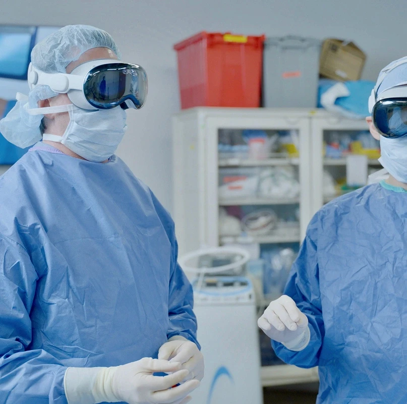 Two surgeons wearing Apple Vision Pro headsets in a hospital operating room