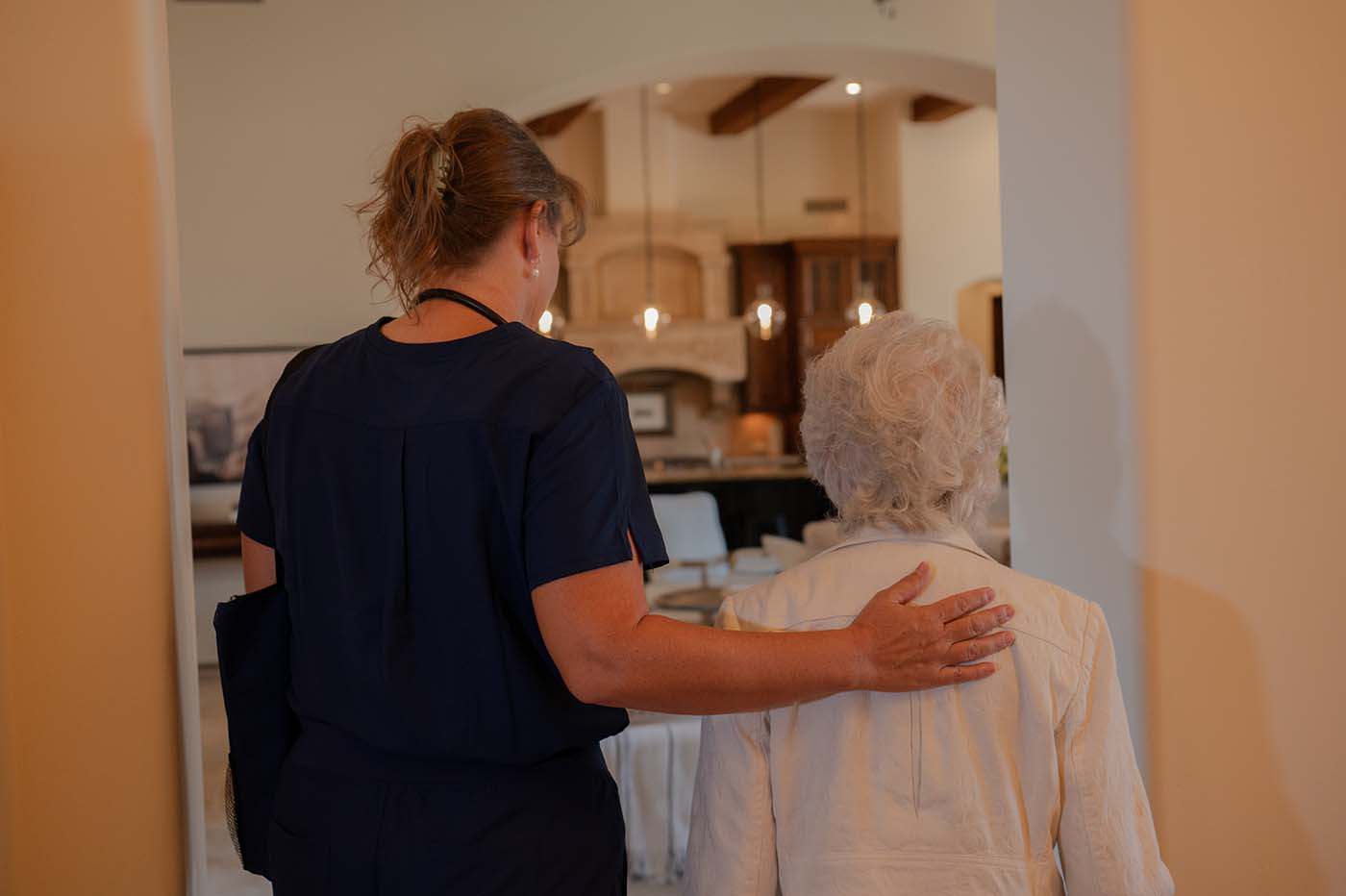 A healthcare professional guides an elderly woman through a home.