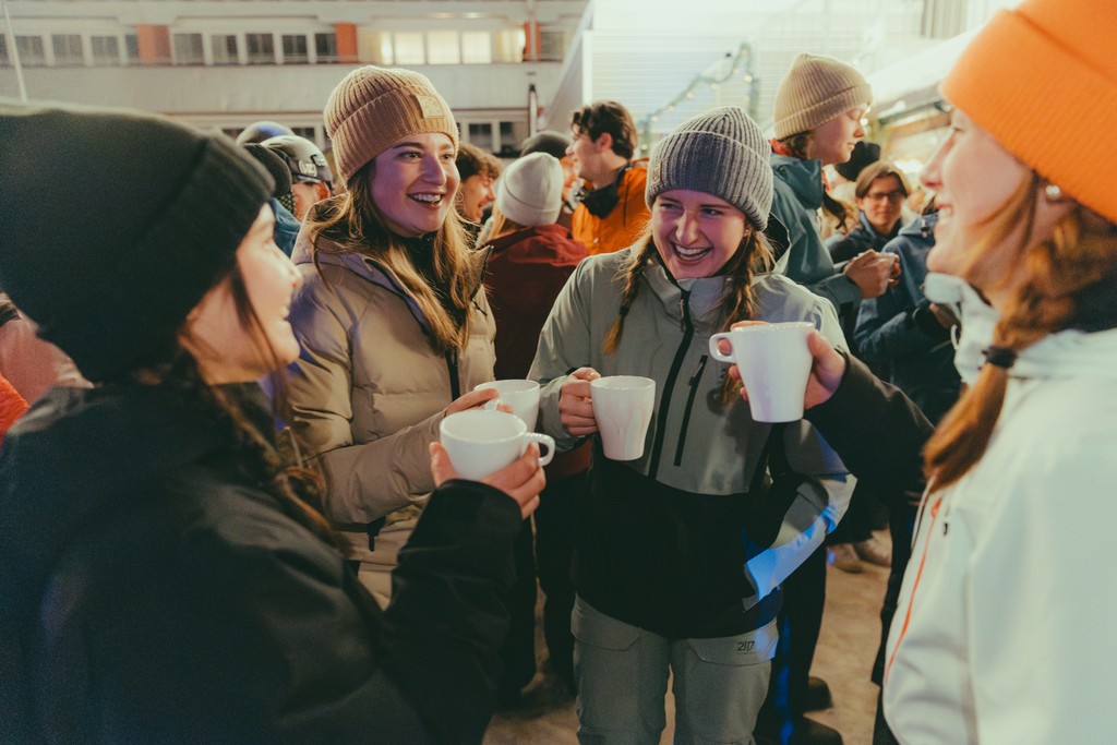 Group of friends enjoying hot drinks in winter clothing outdoors.