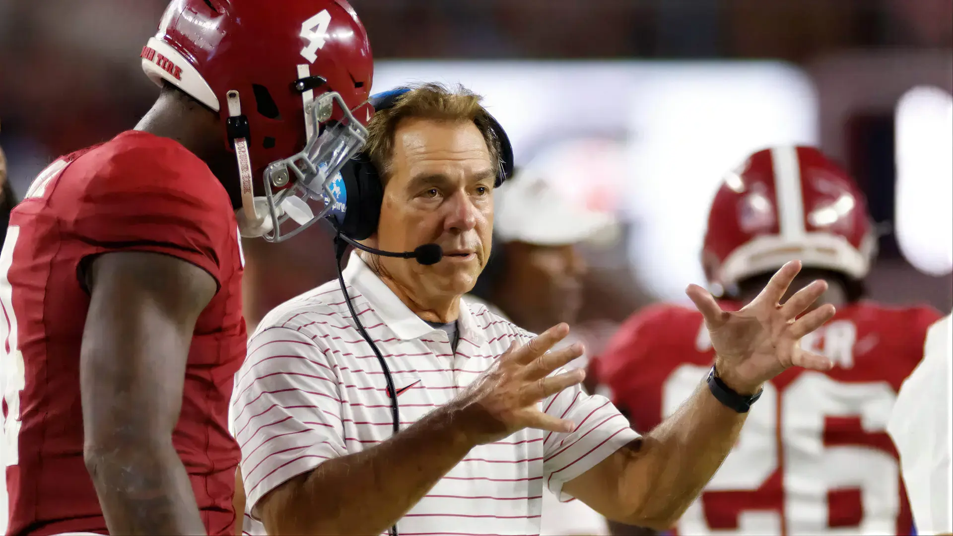 Coach Nick Saban gestures while speaking to Alabama football player during game on sideline.