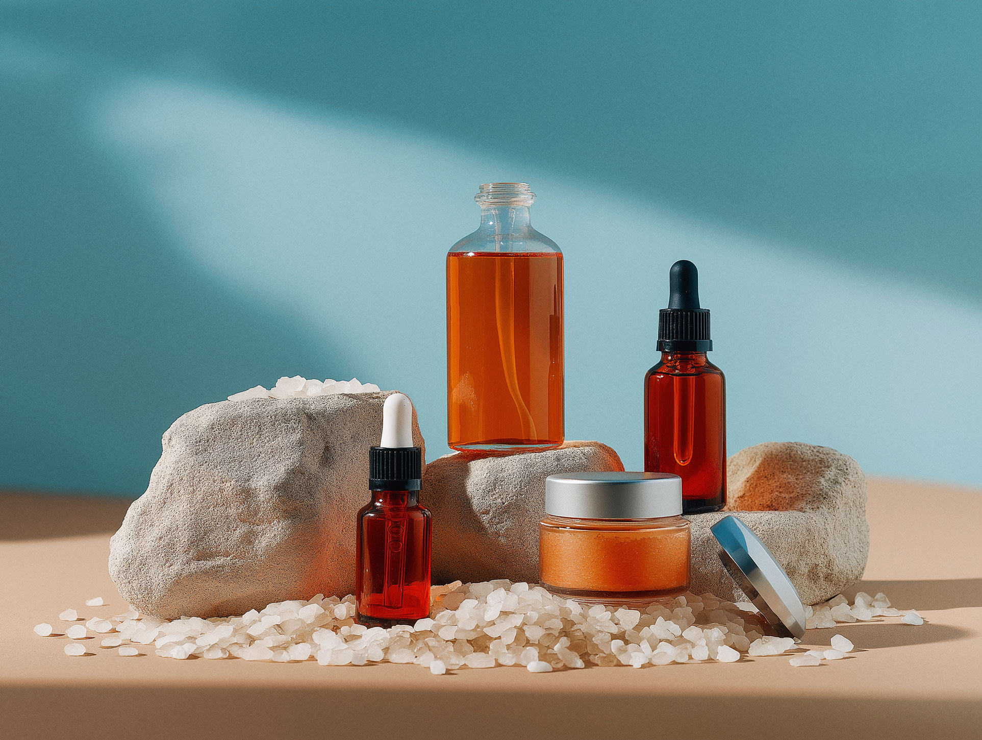 Amber glass skincare bottles and cream jars arranged with natural stones on sandy beach surface