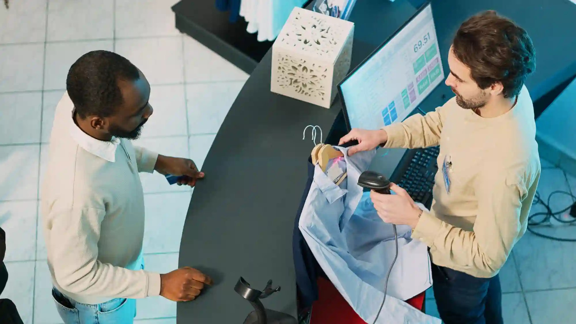 Overhead view of a retail cashier scanning a shirt for a customer at a modern, digital checkout counter.