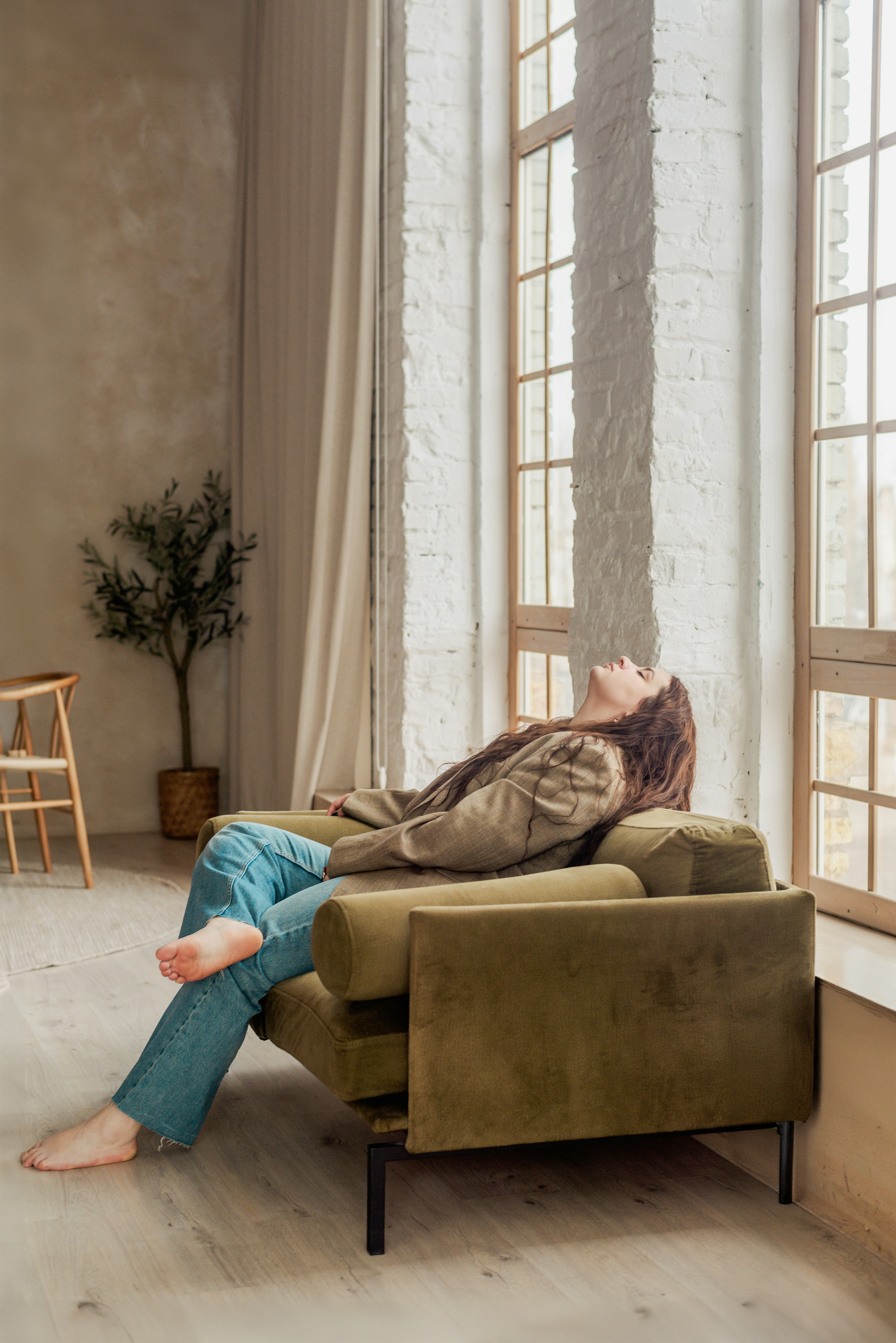 Uma pessoa serena a ouvir áudio com auscultadores, sentada confortavelmente num sofá ou num espaço tranquilo em casa, com luz suave.
