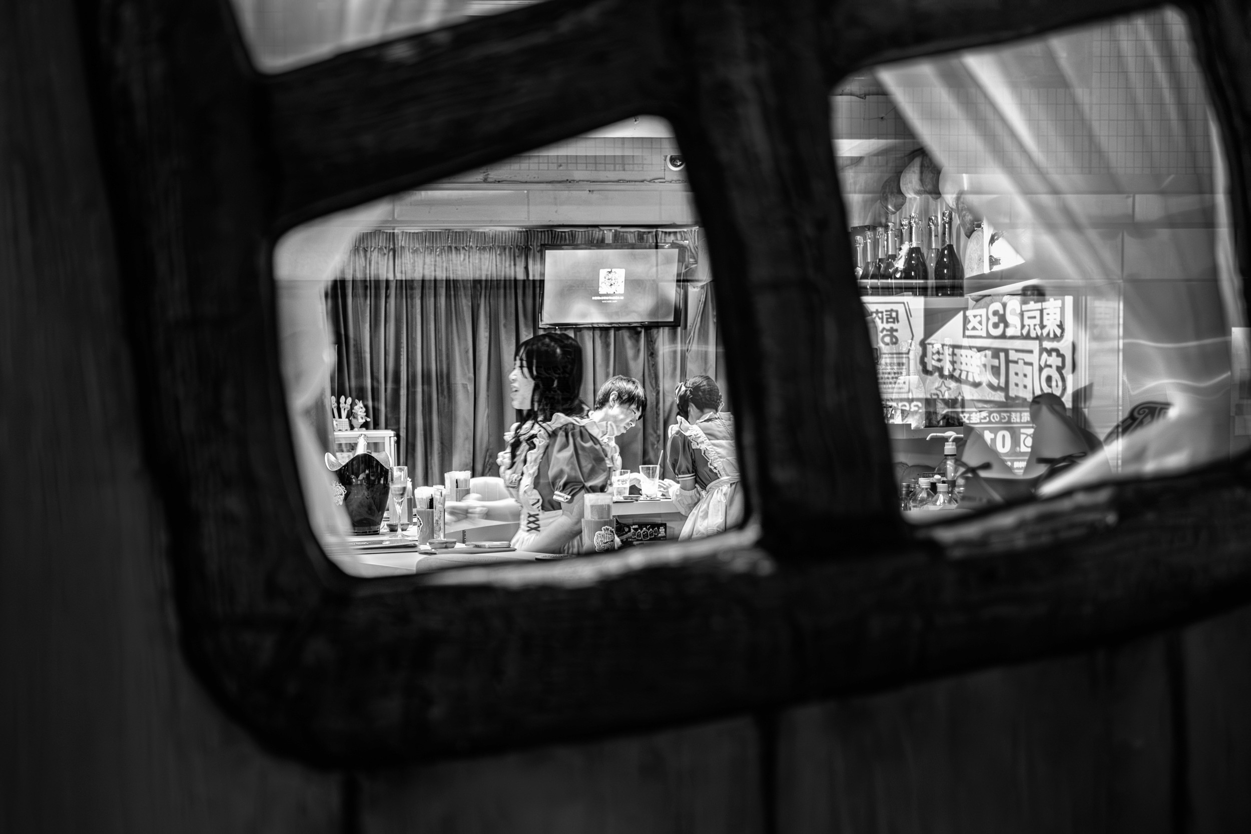 Black and white ambient photograph of people in costume serving drinks through a framed café window.
