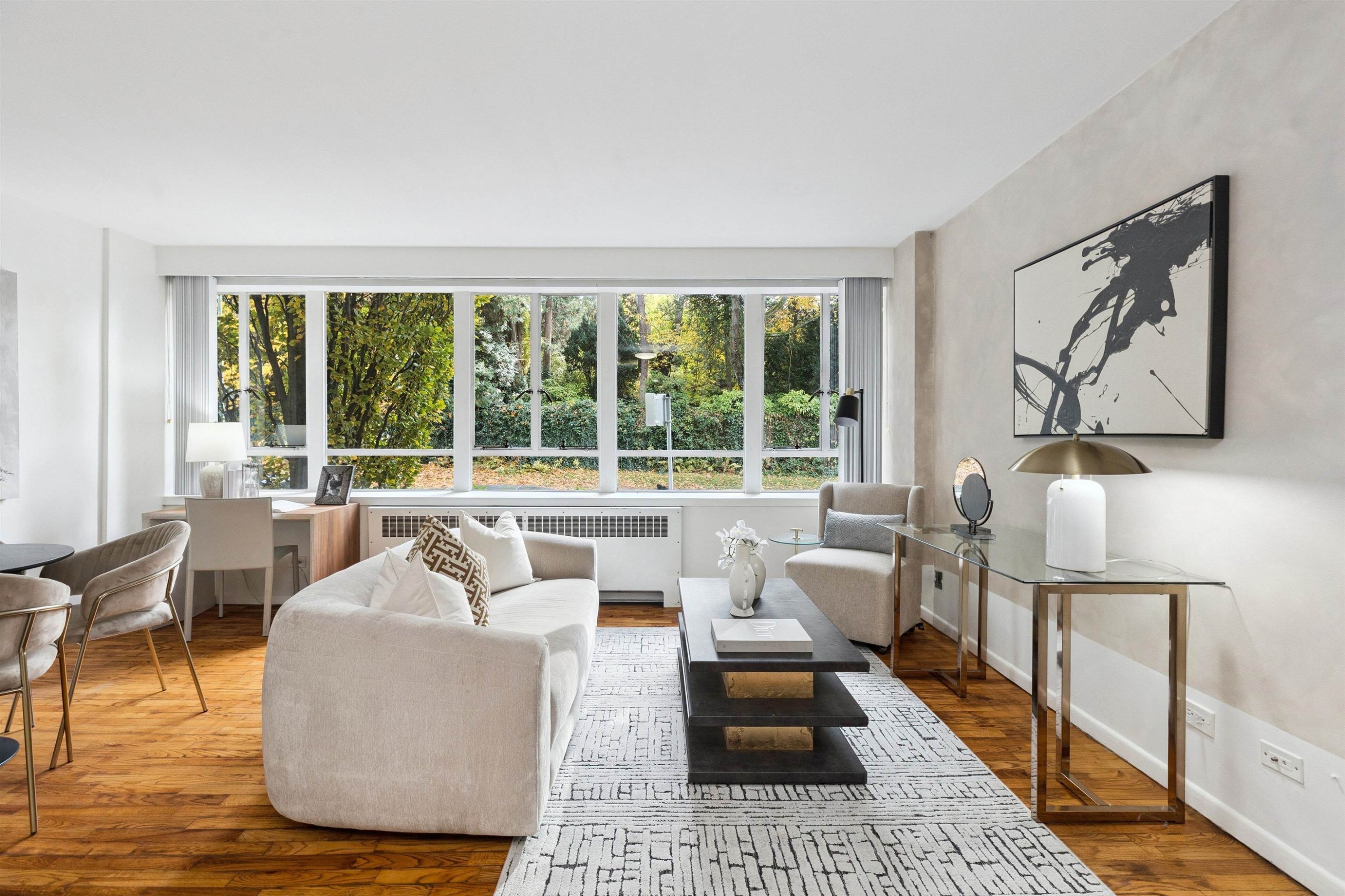Bright, modern living room with large windows, white furniture, and warm wooden flooring.