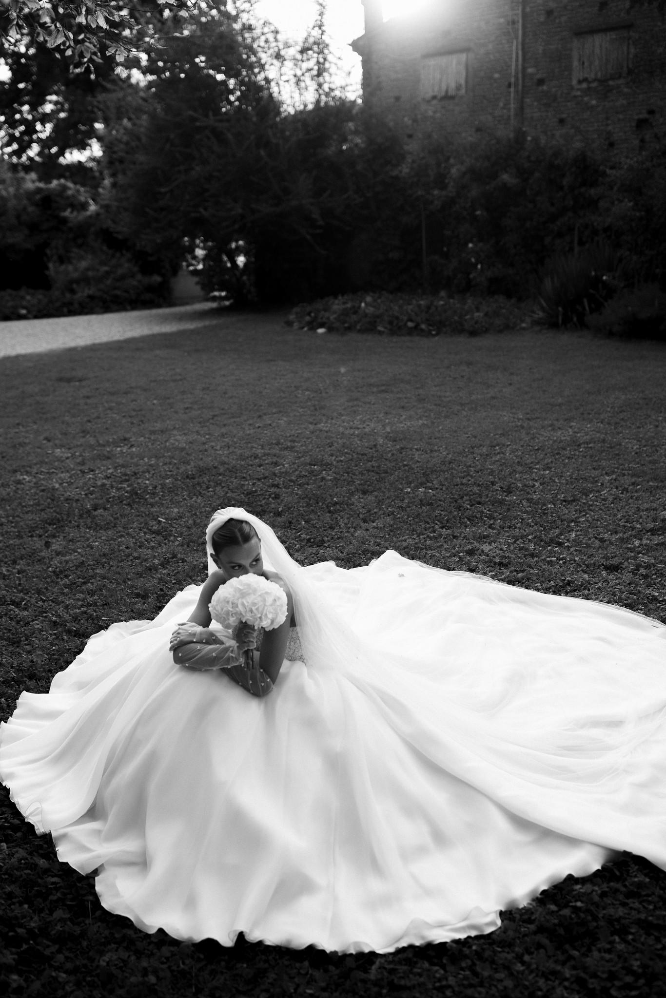 Sposa in abito bianco con velo e bouquet nel parco di Villa Ferrari, reportage matrimoniale in bianco e nero