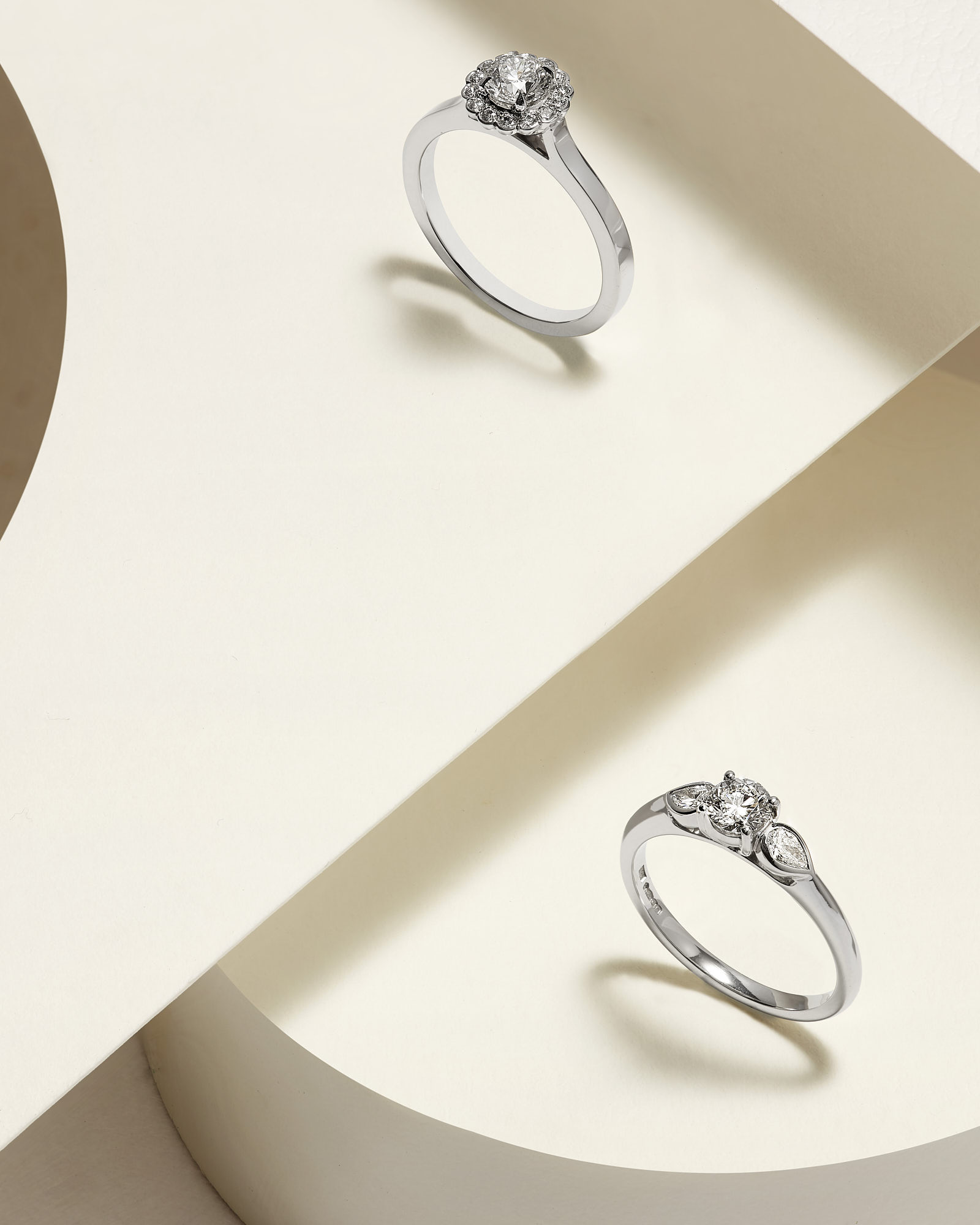 Elegant silver diamond engagement rings on minimalist beige background.