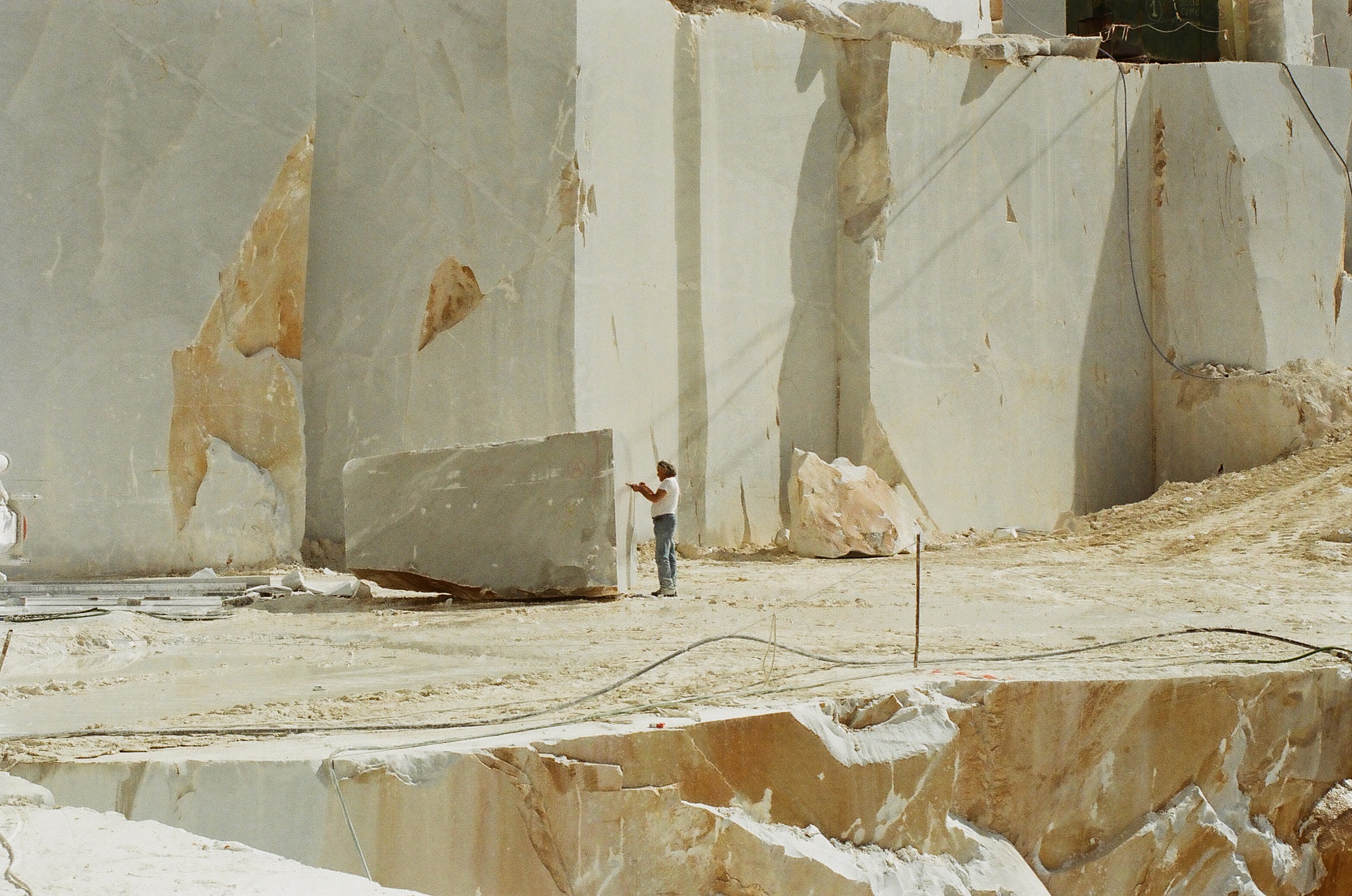 Un ouvrier de chantier d'une carrière de marbre face à un gros bloc de marbre qui a été extrait de la montagne de marbre en arrière plan