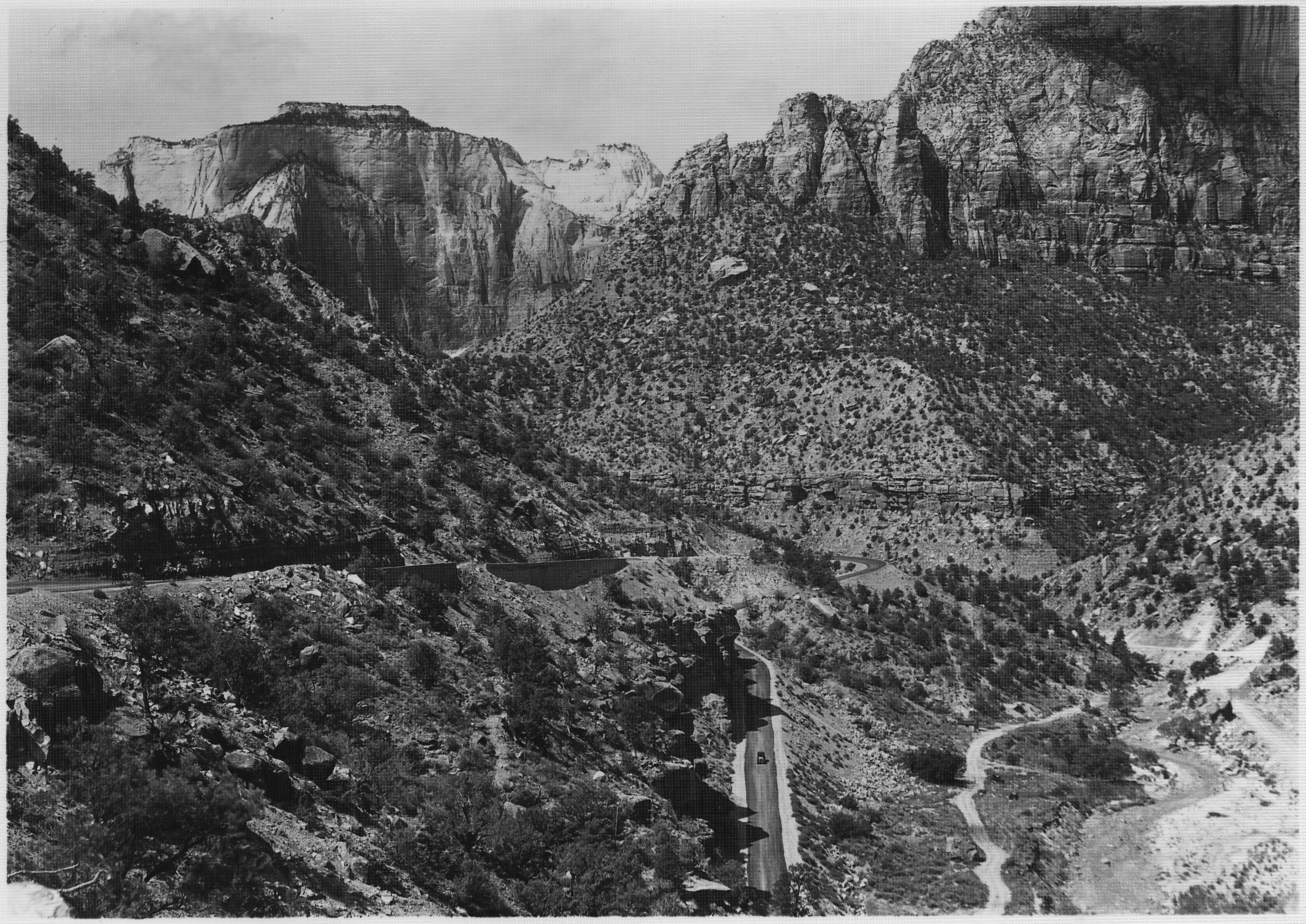 Historic black and white photograph of the switchbacks on the Mount Carmel road west of the Zion tunnel, with the West Temple rising at the left.