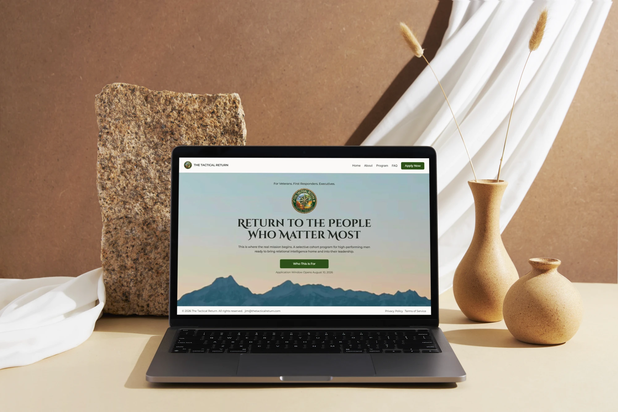 A laptop computer displaying the minimalist homepage of The Tactical Return website against a warm, earthy background with decorative rocks and ceramic vases.